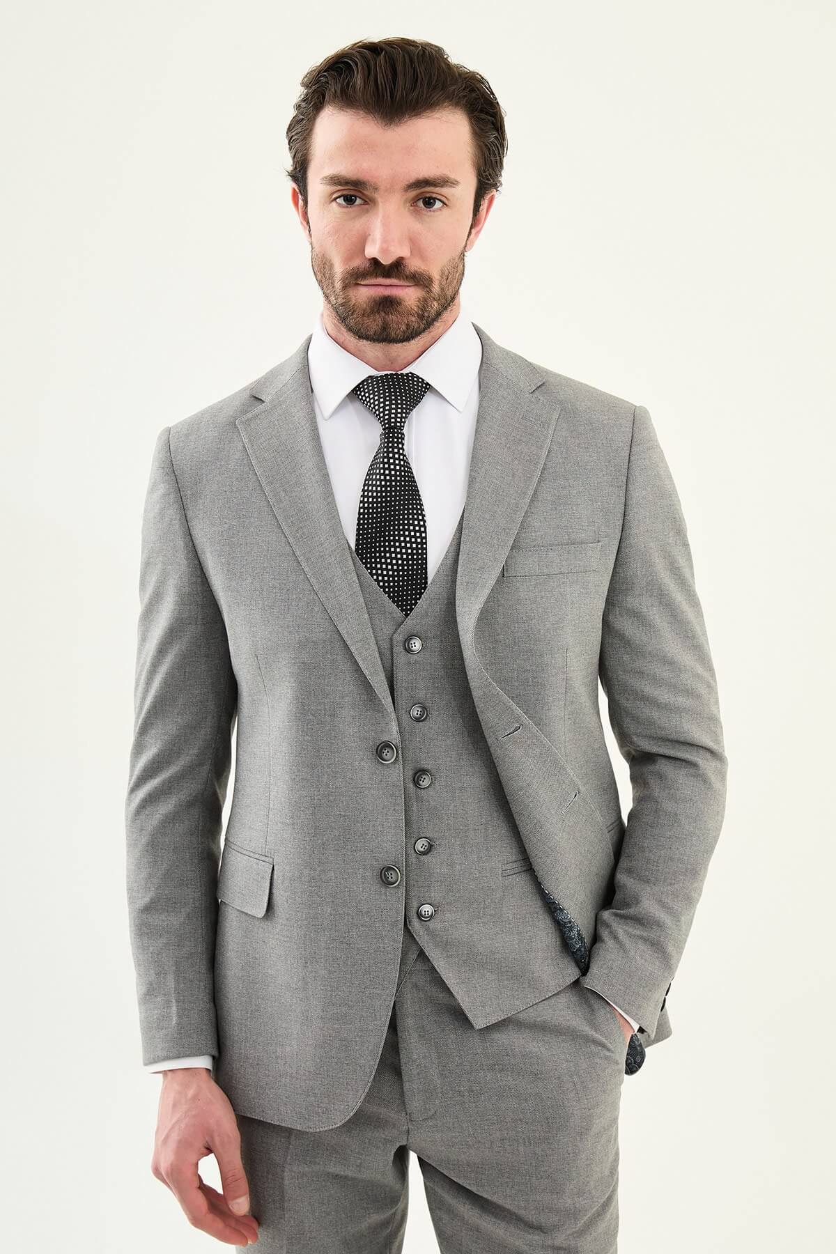 Man wearing a gray three-piece slim fit suit, including jacket, vest, and trousers, paired with a white dress shirt and black patterned tie