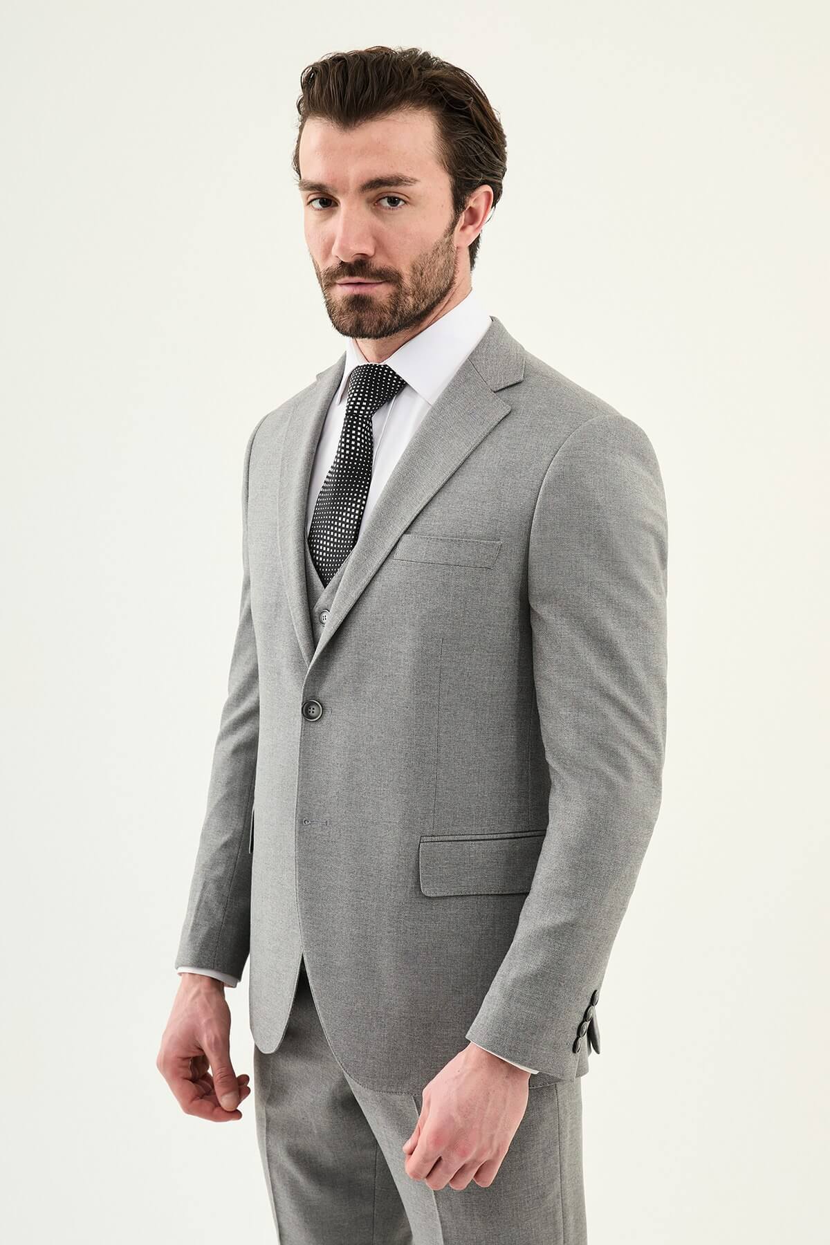 Man wearing a gray three-piece slim fit suit, including jacket, vest, and trousers, paired with a white dress shirt and black patterned tie