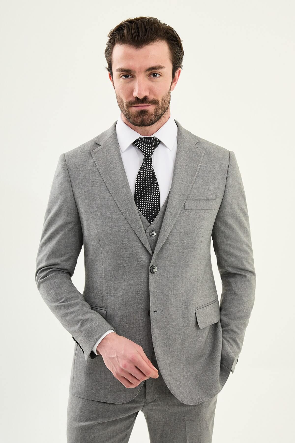 Man wearing a gray three-piece slim fit suit, including jacket, vest, and trousers, paired with a white dress shirt and black patterned tie