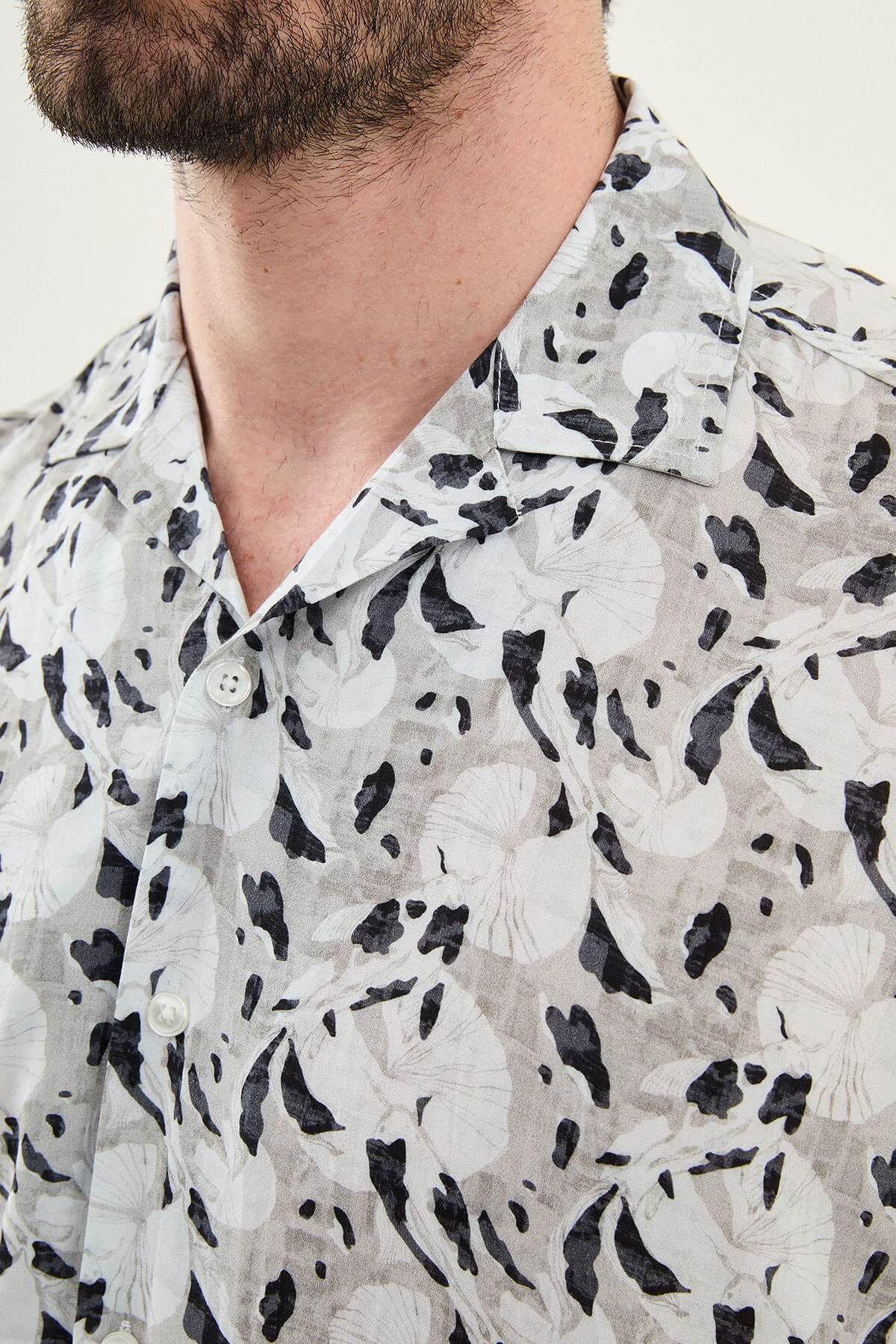Man wearing a gray patterned short-sleeve summer shirt, front view, styled with casual summer trousers, neutral background.