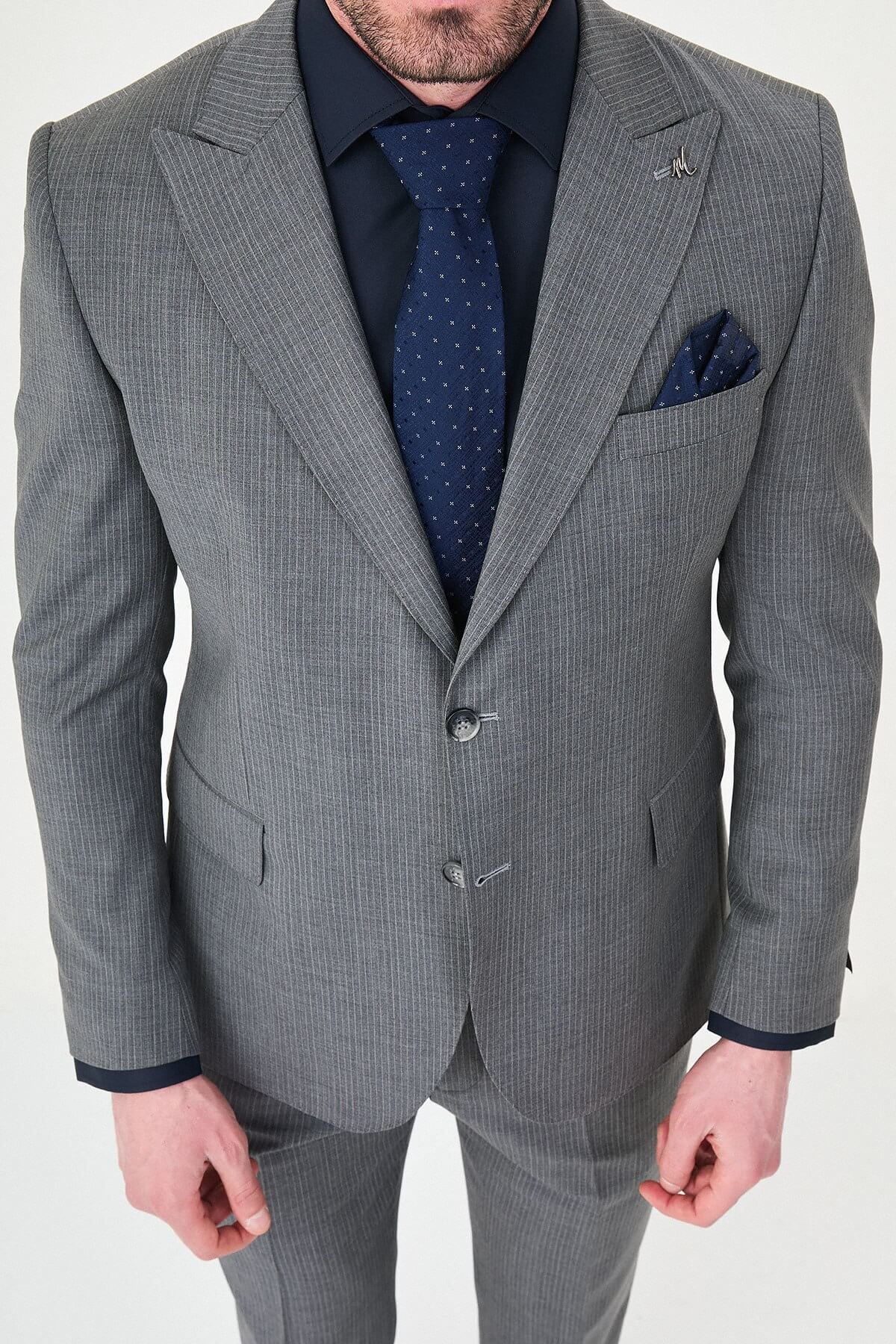 man wearing a gray slim fit wool suit with wide collar, paired with a navy shirt and matching tie.