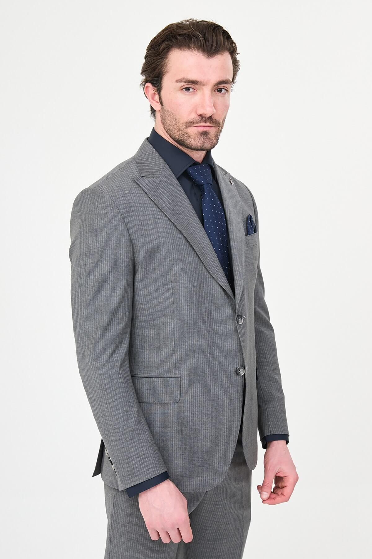 man wearing a gray slim fit wool suit with wide collar, paired with a navy shirt and matching tie.