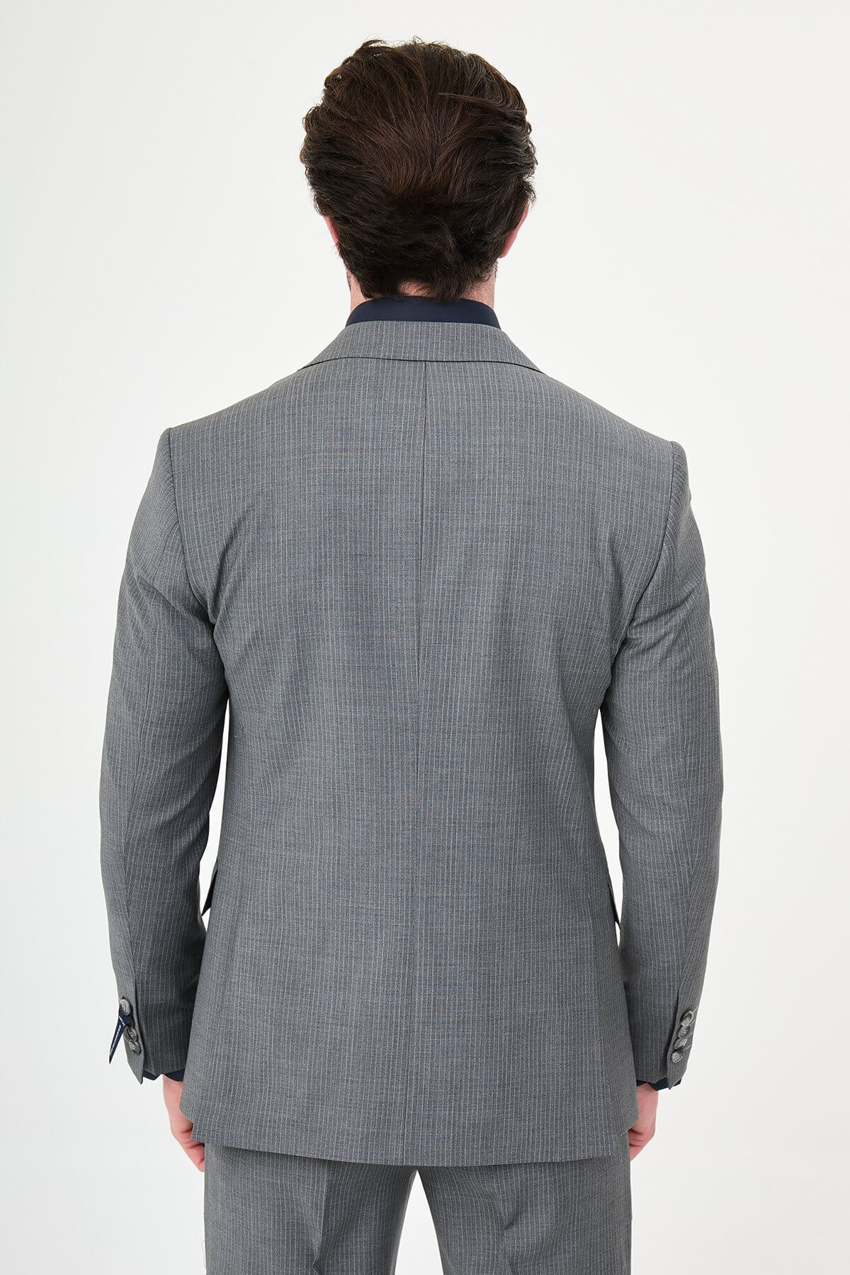 man wearing a gray slim fit wool suit with wide collar, paired with a navy shirt and matching tie.