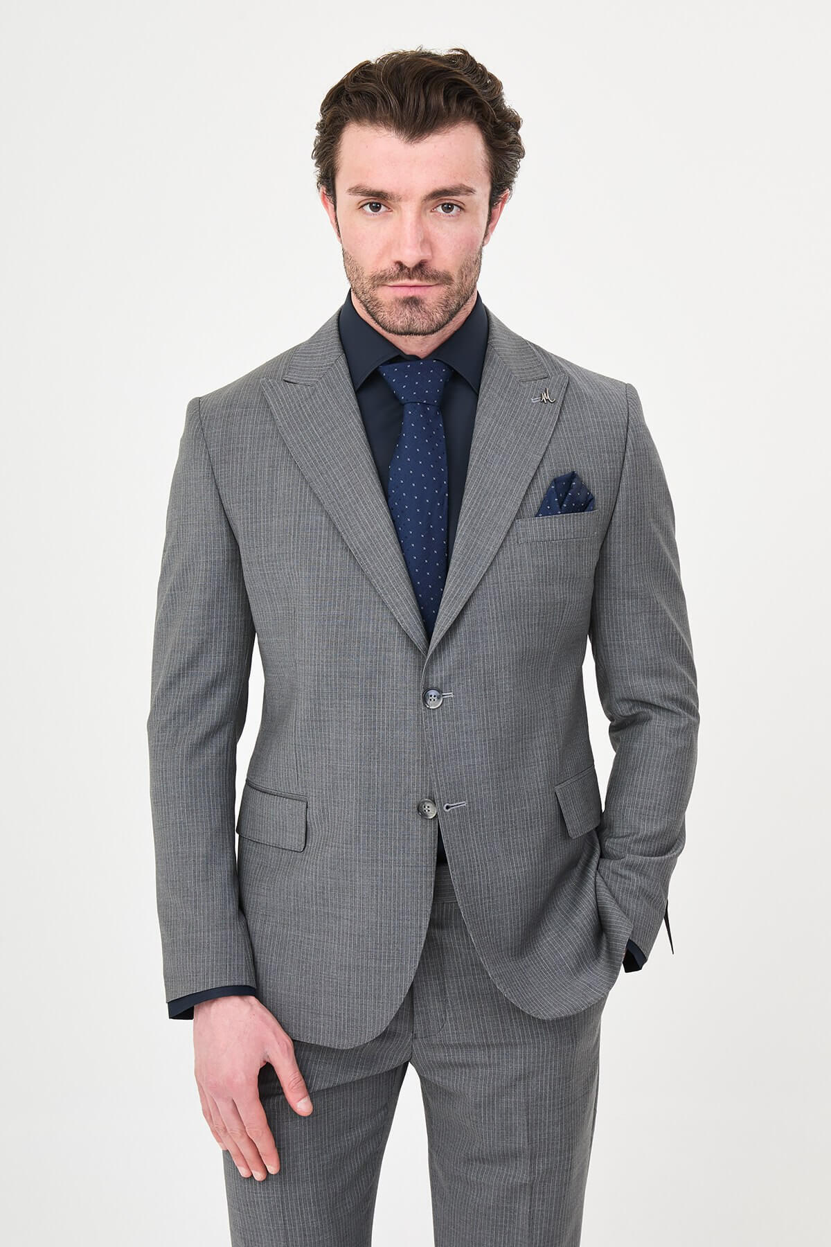 man wearing a gray slim fit wool suit with wide collar, paired with a navy shirt and matching tie.