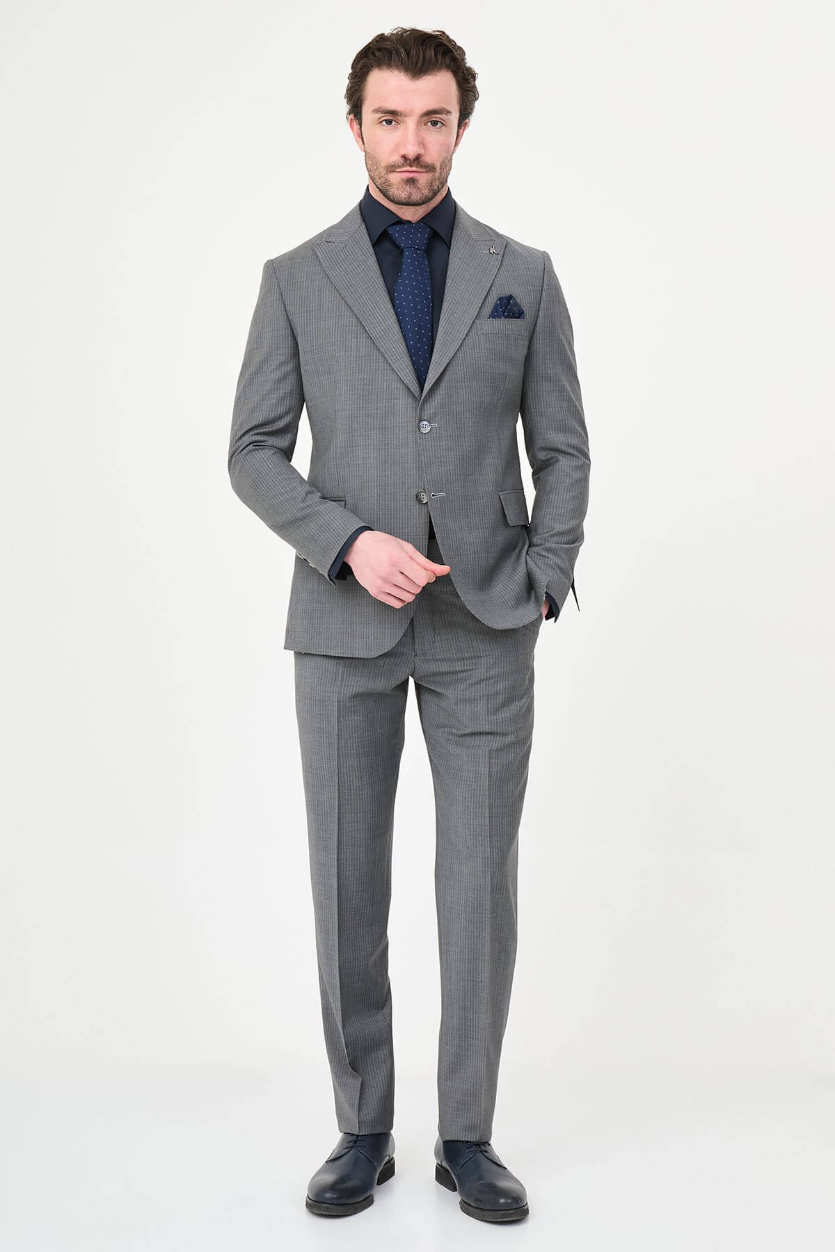 man wearing a gray slim fit wool suit with wide collar, paired with a navy shirt and matching tie.