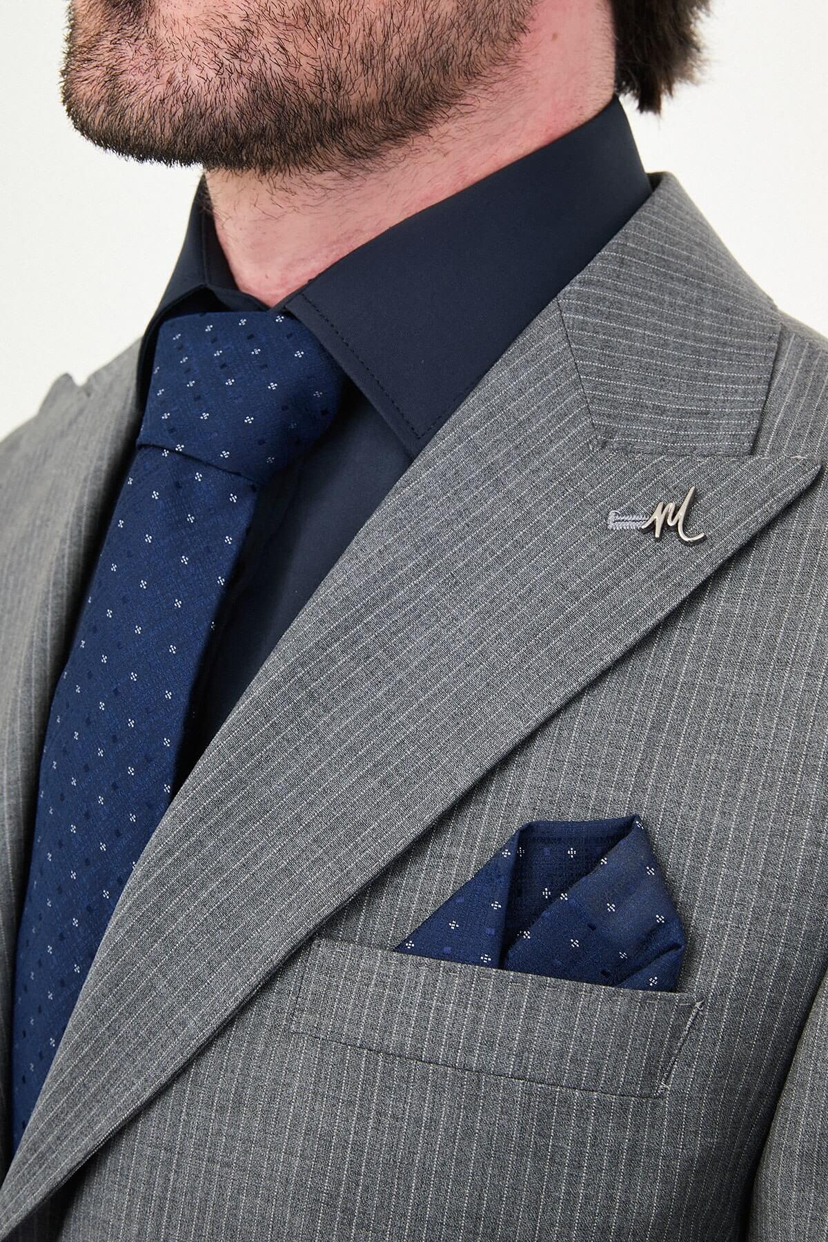 man wearing a gray slim fit wool suit with wide collar, paired with a navy shirt and matching tie.