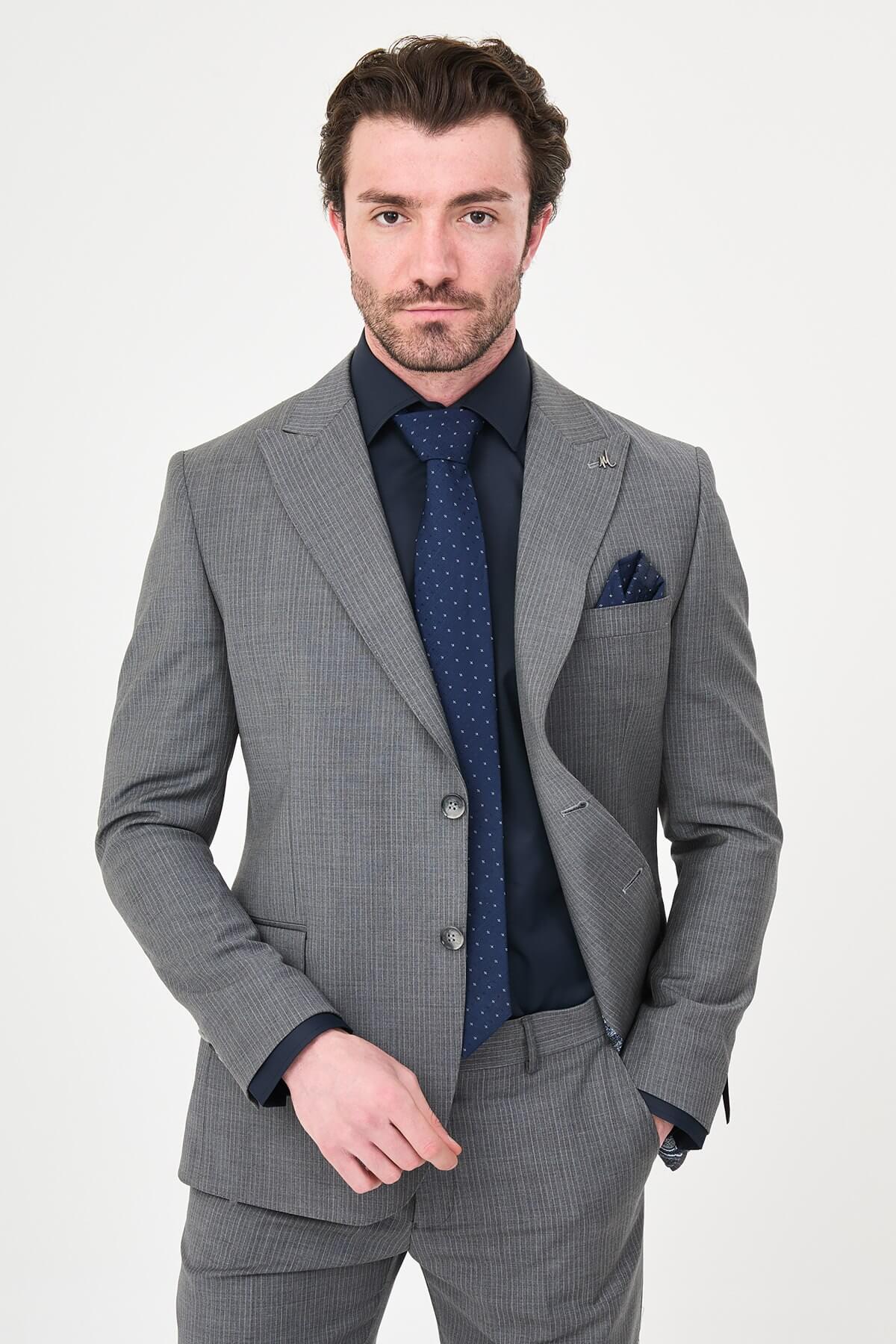 man wearing a gray slim fit wool suit with wide collar, paired with a navy shirt and matching tie.