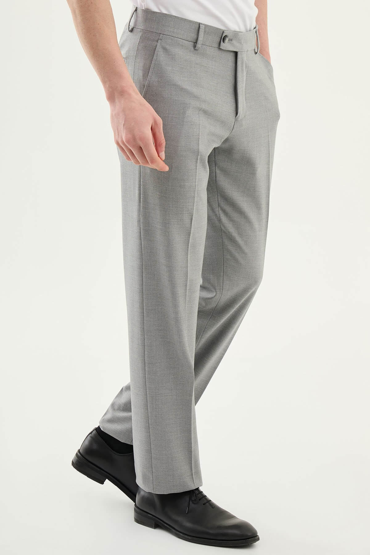 Man wearing gray pleated dress trousers with a straight slim fit, styled with a white dress shirt and black leather shoes.