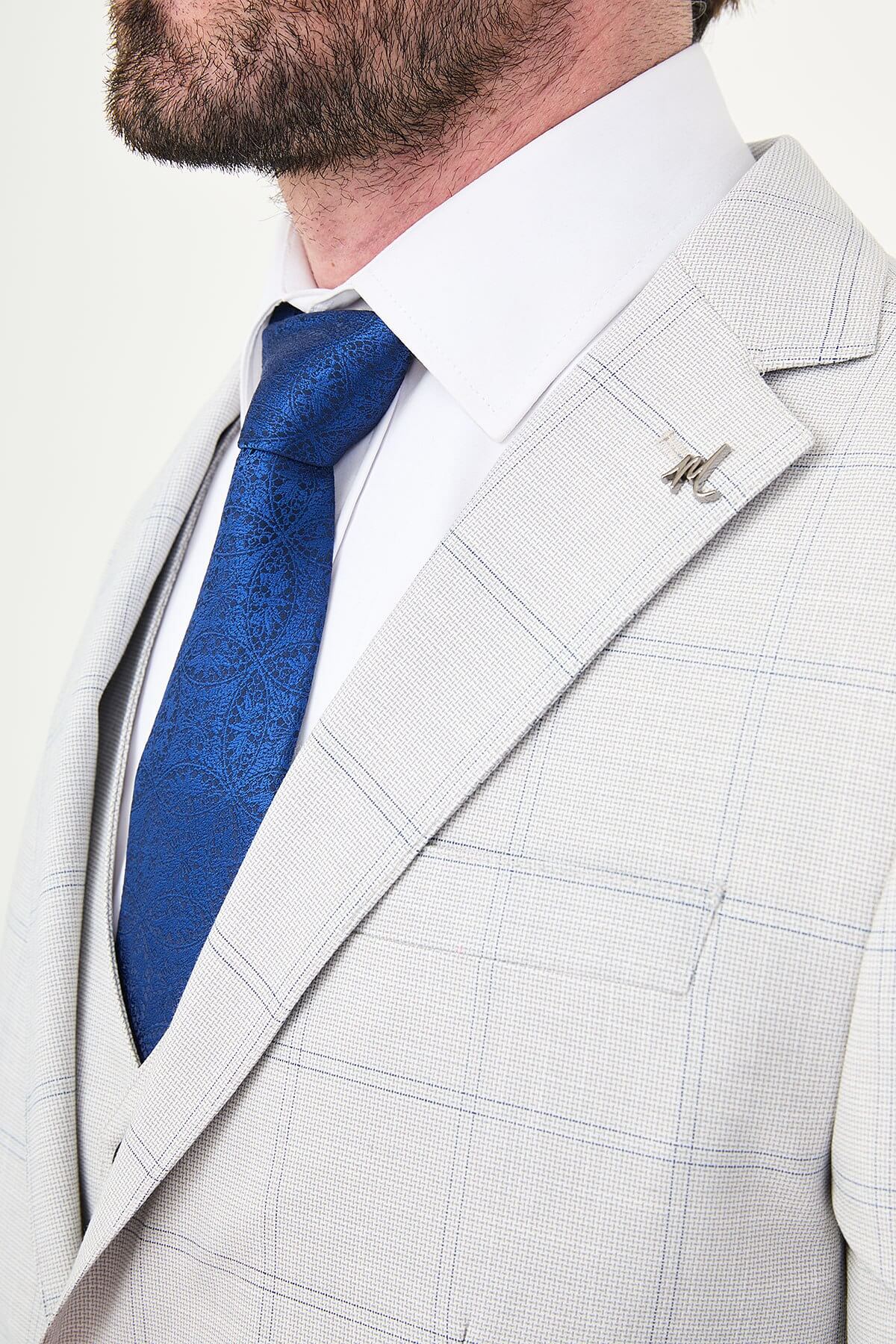 a gray check slim-fit three-piece suit with matching waistcoat and trousers, white dress shirt, royal-blue tie, and black leather Derby shoes.