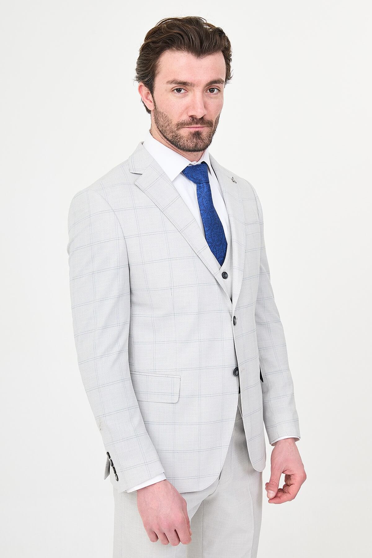 a gray check slim-fit three-piece suit with matching waistcoat and trousers, white dress shirt, royal-blue tie, and black leather Derby shoes.