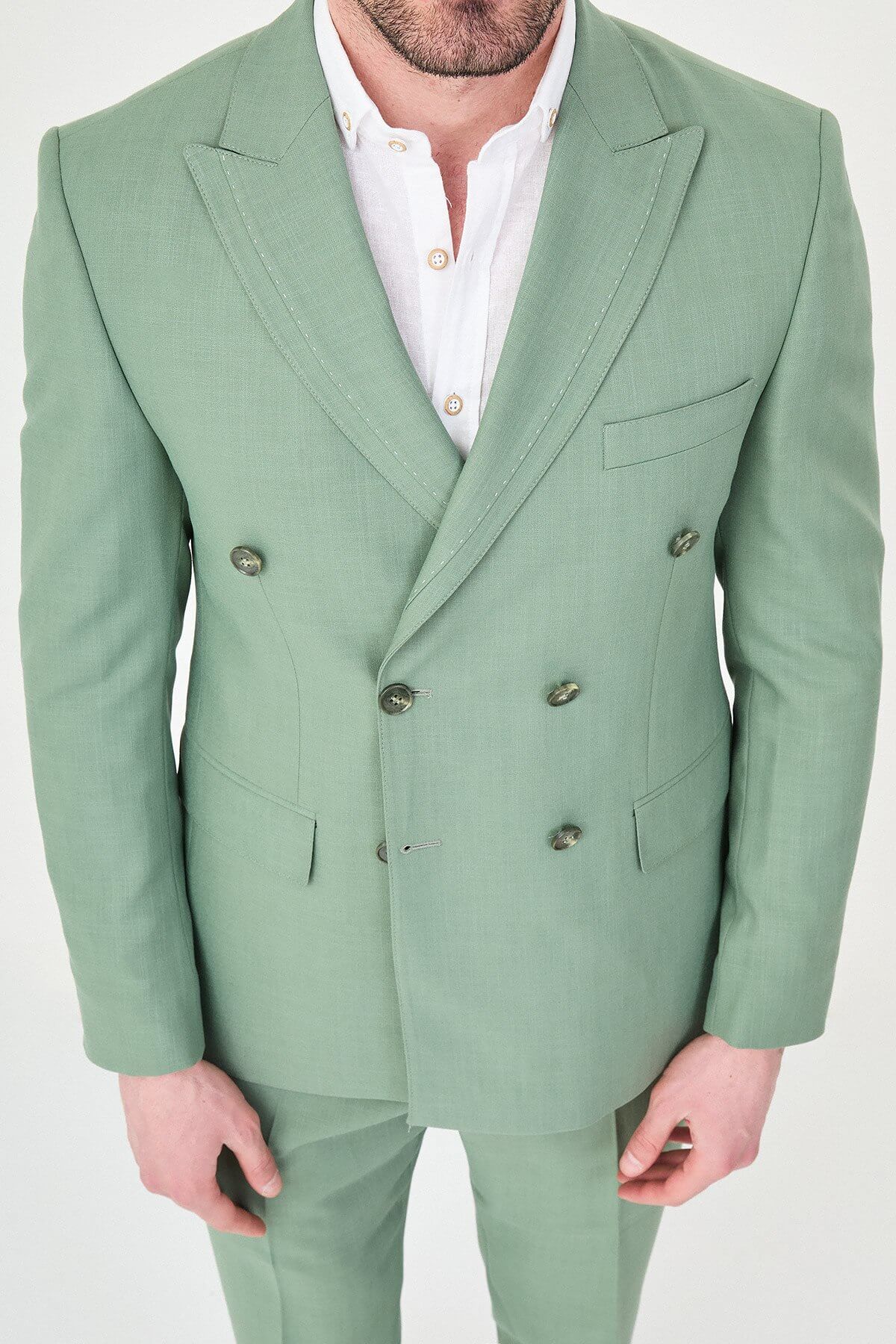 a green slim-fit double-breasted linen-blend suit with peak lapels, matching trousers, an open-collar white shirt, and white leather sneakers.