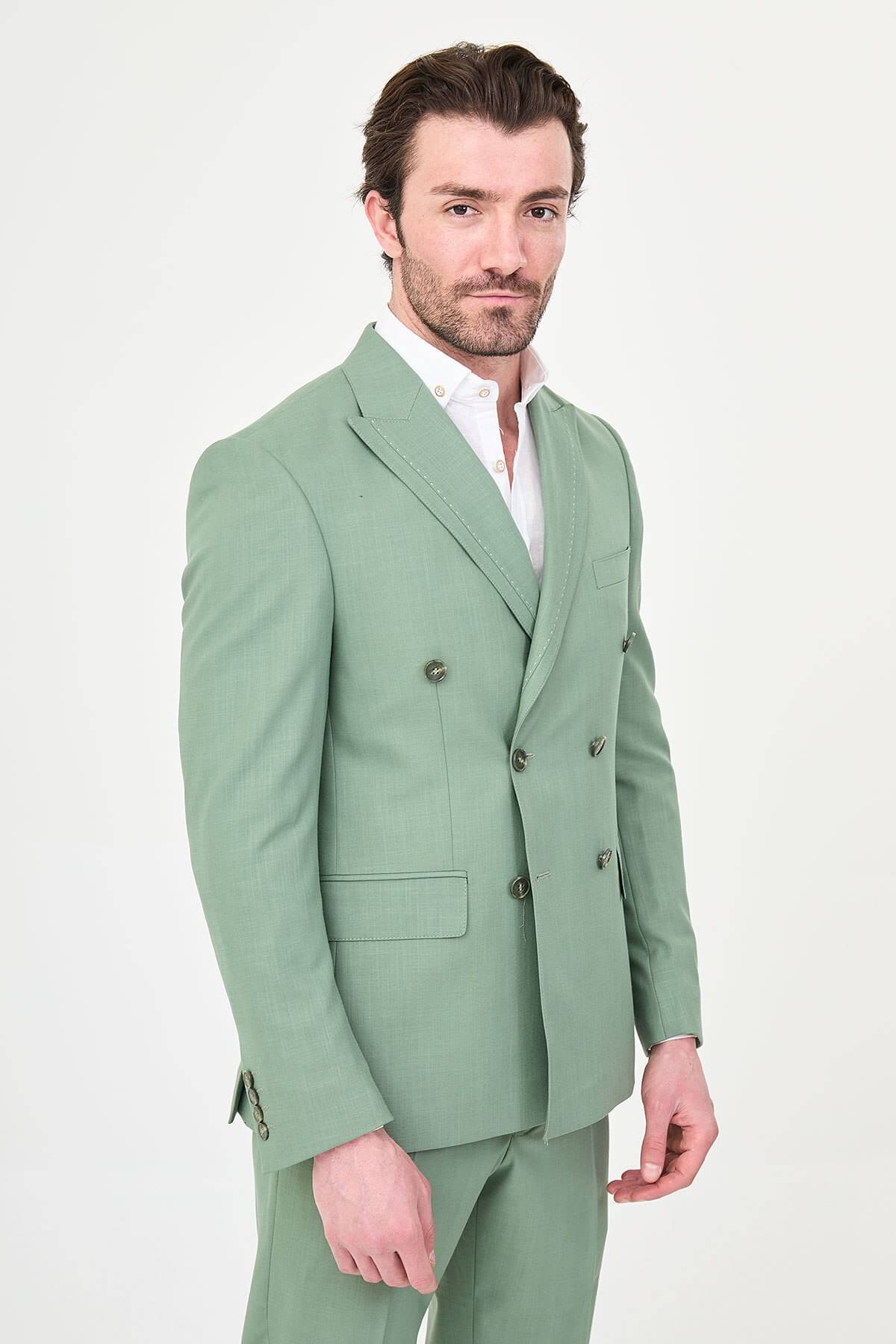 a green slim-fit double-breasted linen-blend suit with peak lapels, matching trousers, an open-collar white shirt, and white leather sneakers.
