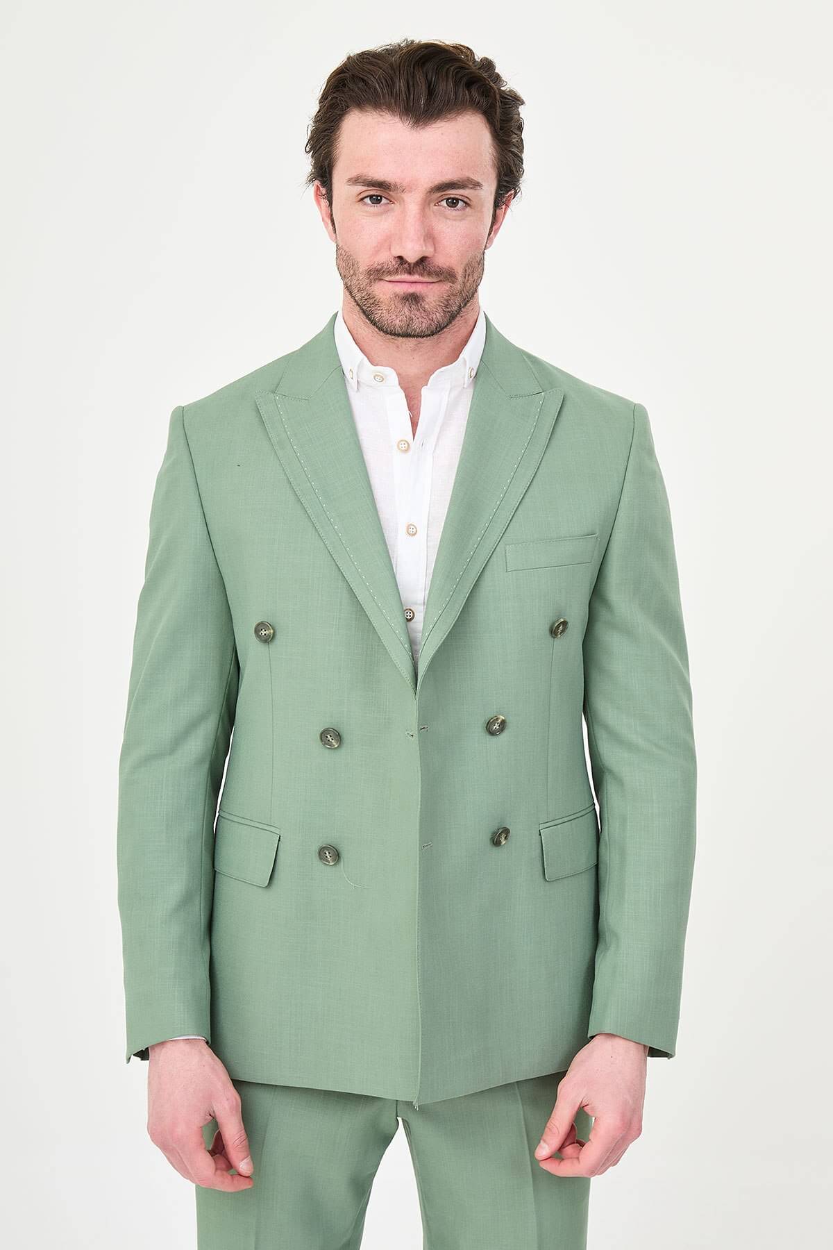 a green slim-fit double-breasted linen-blend suit with peak lapels, matching trousers, an open-collar white shirt, and white leather sneakers.
