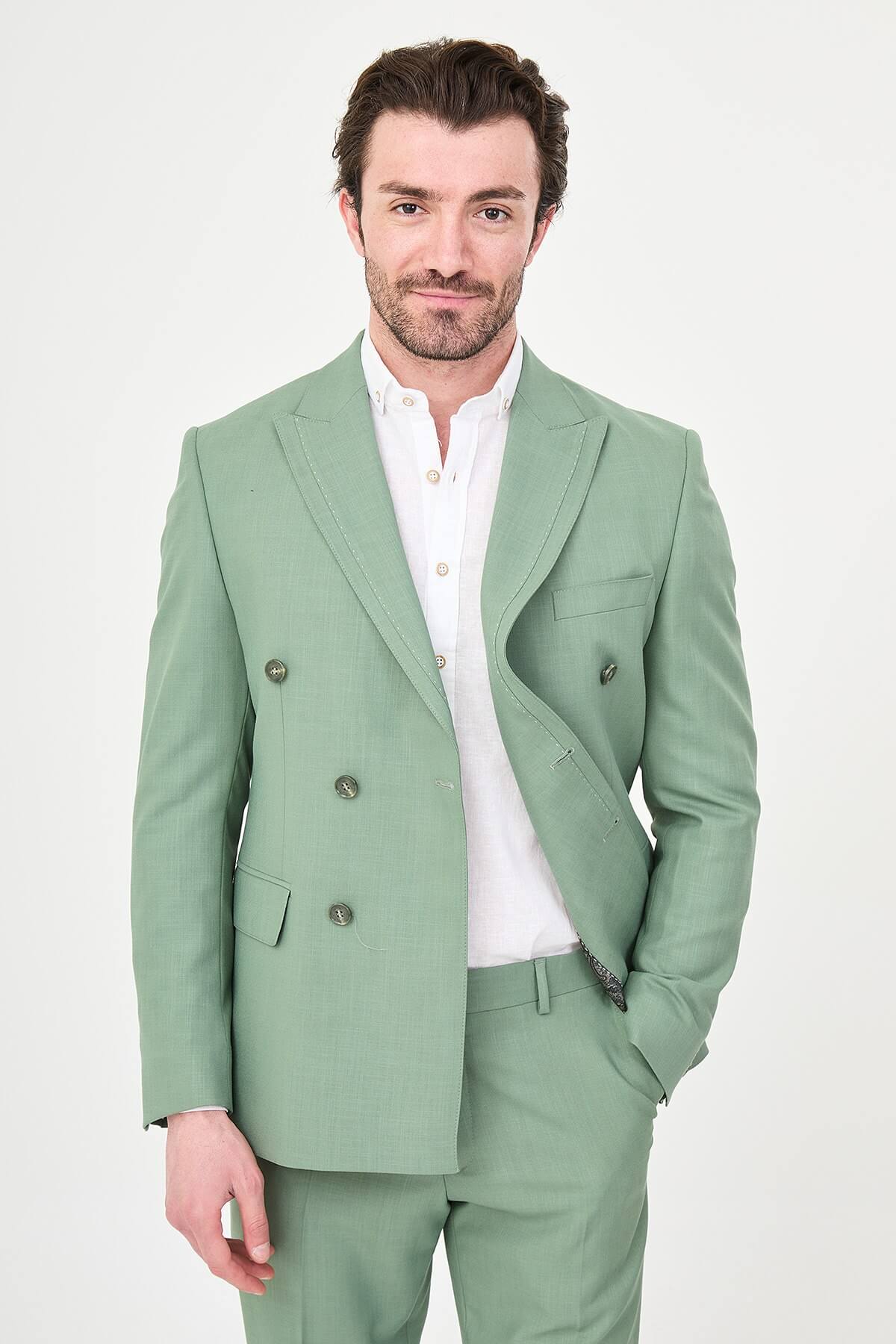 a green slim-fit double-breasted linen-blend suit with peak lapels, matching trousers, an open-collar white shirt, and white leather sneakers.