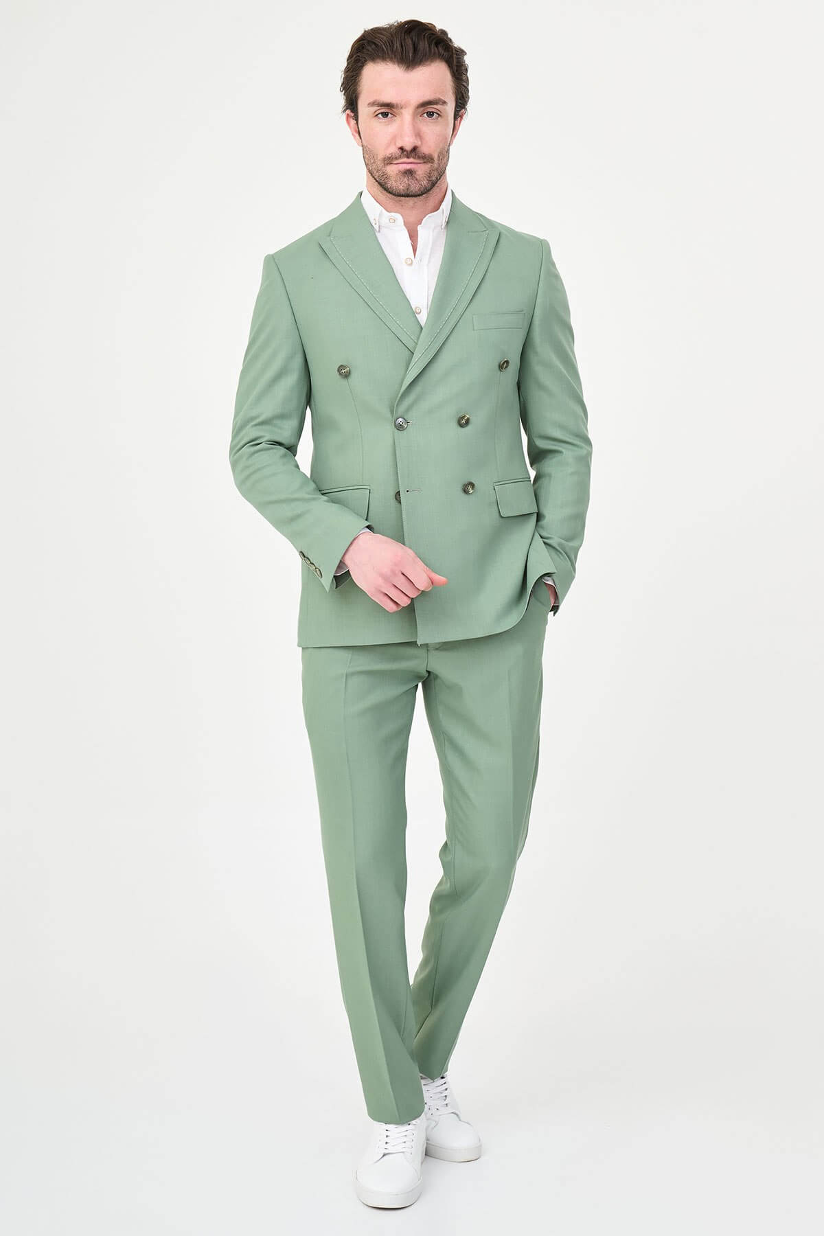 a green slim-fit double-breasted linen-blend suit with peak lapels, matching trousers, an open-collar white shirt, and white leather sneakers.