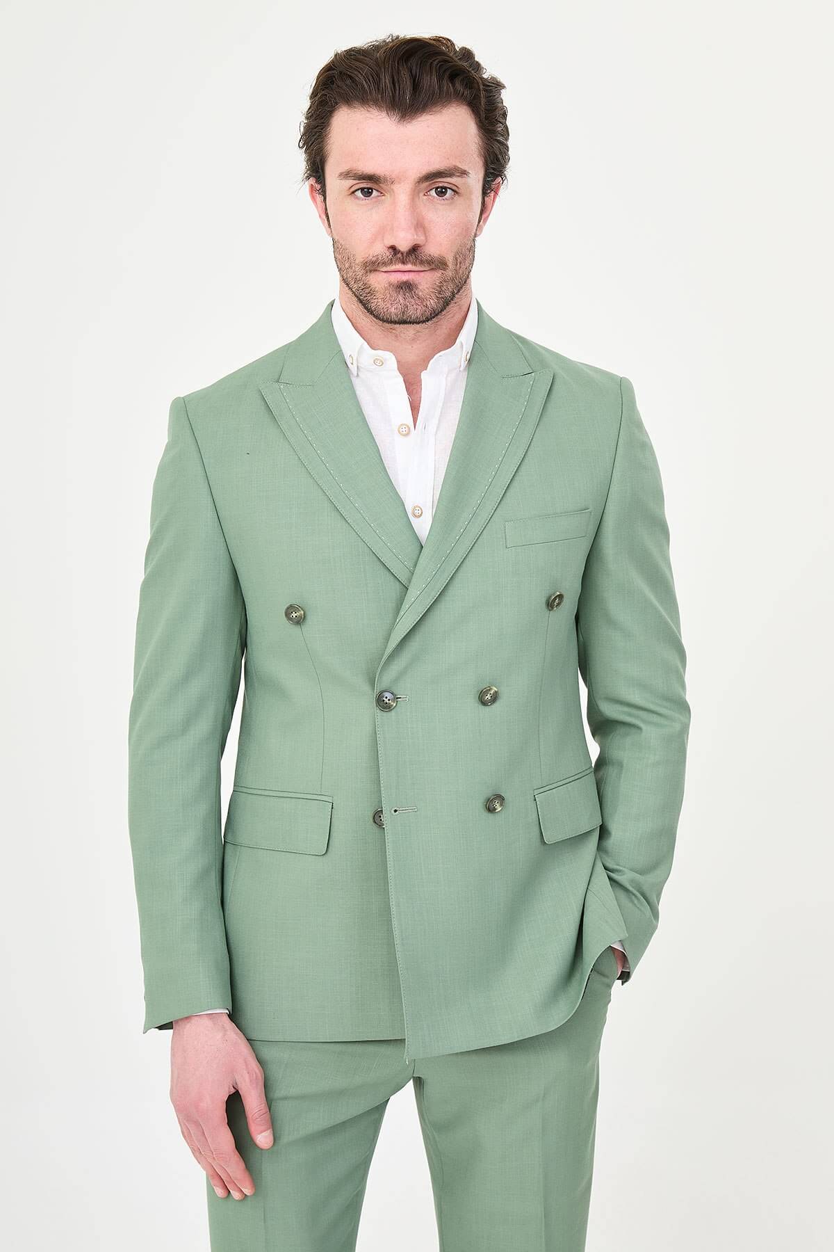 a green slim-fit double-breasted linen-blend suit with peak lapels, matching trousers, an open-collar white shirt, and white leather sneakers.