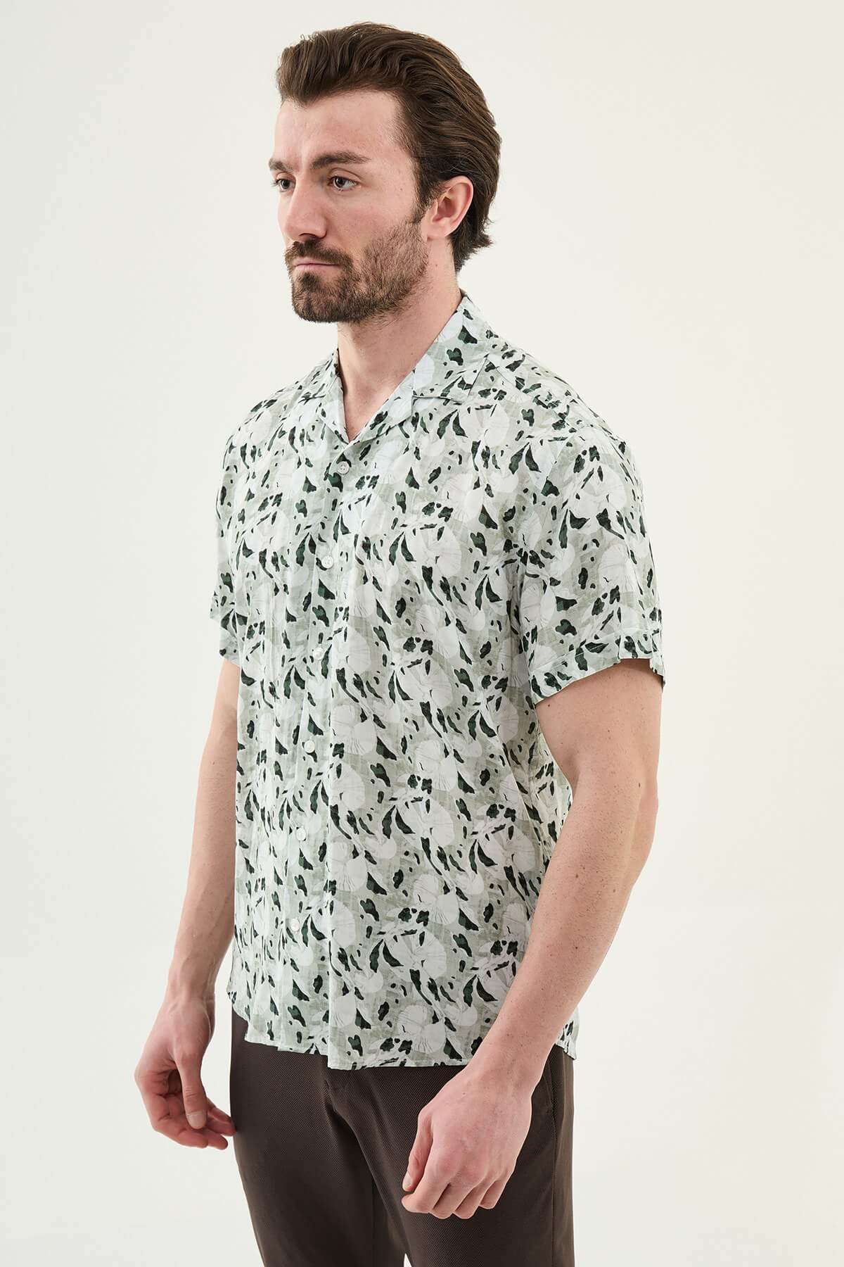 Men wearing a green patterned short-sleeve summer shirt with tropical floral and leaf print, styled casually with light summer trousers.