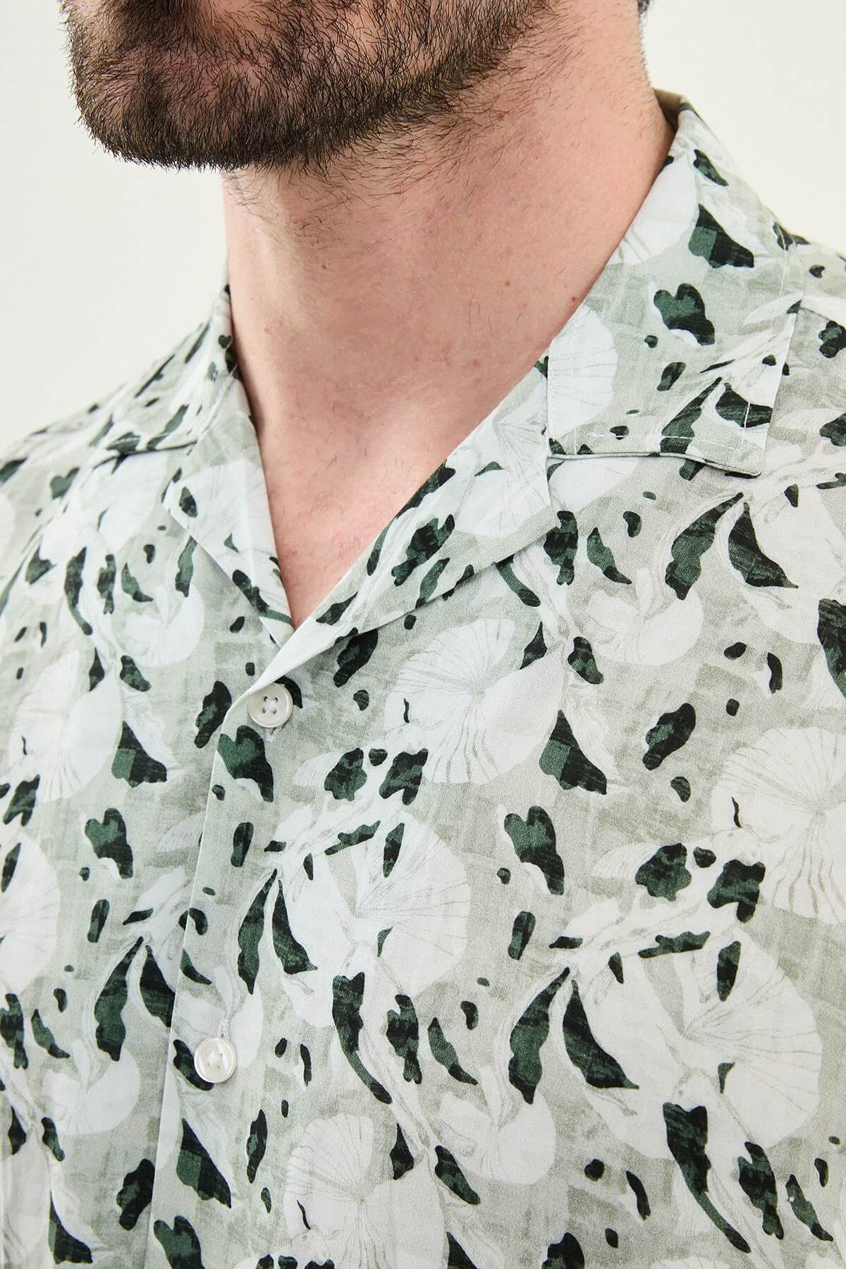 Men wearing a green patterned short-sleeve summer shirt with tropical floral and leaf print, styled casually with light summer trousers.