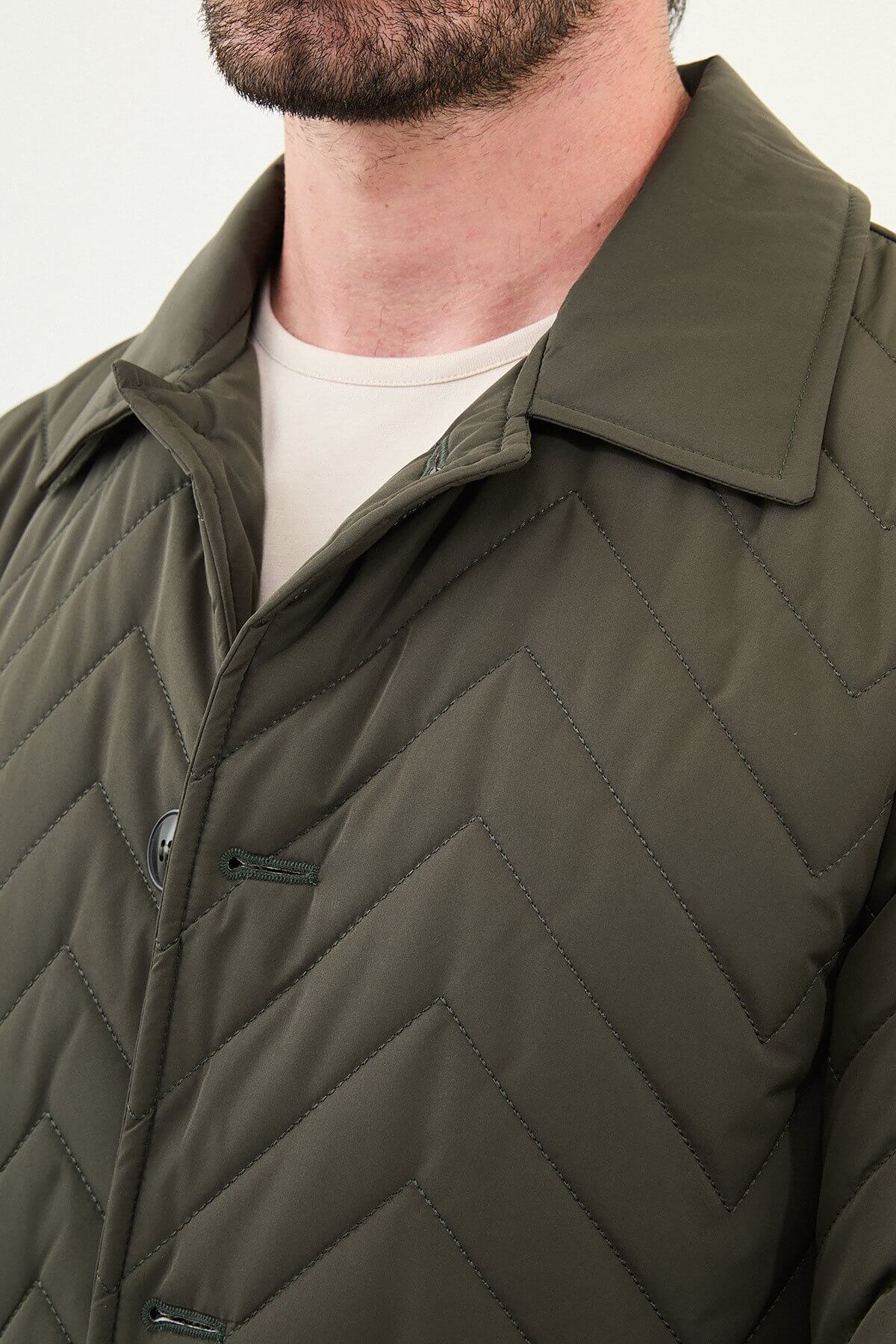 Man wearing a slim fit green quilted car coat with button closure, styled with brown trousers and beige sneakers.