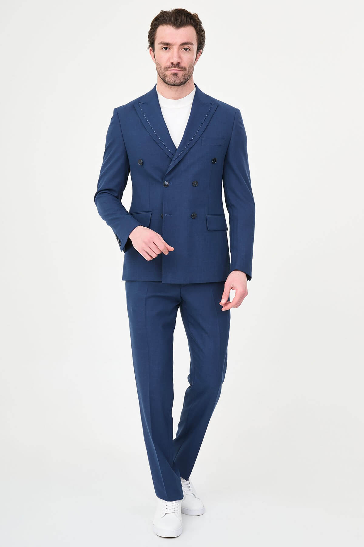 an indigo slim-fit double-breasted linen-blend suit with peak lapels, contrast pick stitching, matching trousers, a white knit top, and white leather sneakers.