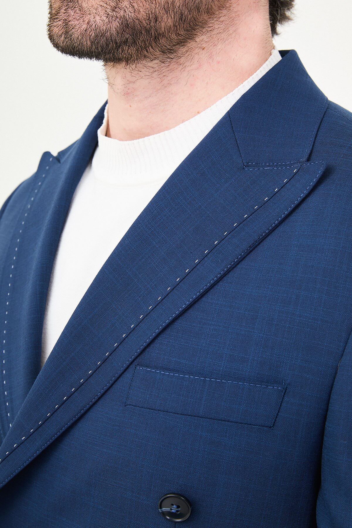 an indigo slim-fit double-breasted linen-blend suit with peak lapels, contrast pick stitching, matching trousers, a white knit top, and white leather sneakers.