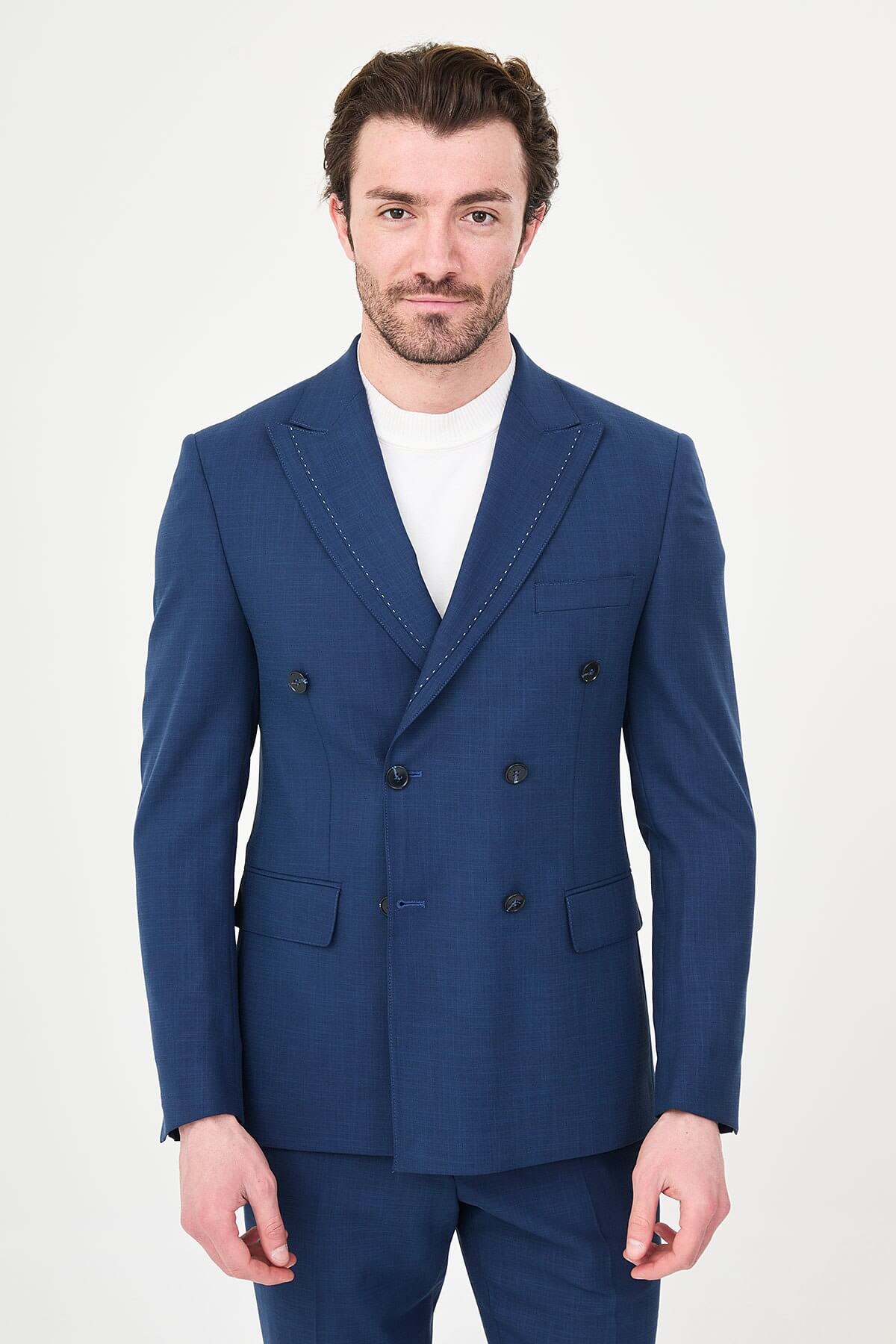 an indigo slim-fit double-breasted linen-blend suit with peak lapels, contrast pick stitching, matching trousers, a white knit top, and white leather sneakers.