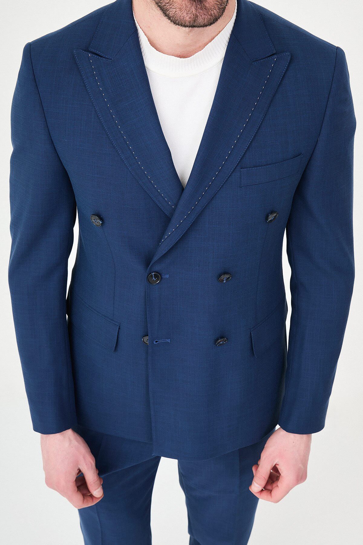 an indigo slim-fit double-breasted linen-blend suit with peak lapels, contrast pick stitching, matching trousers, a white knit top, and white leather sneakers.
