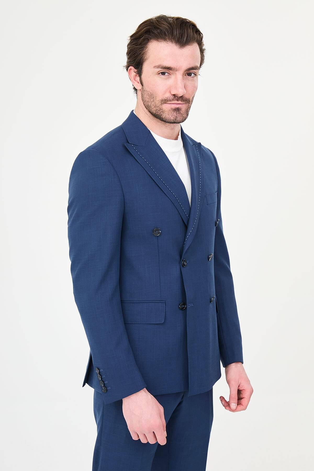 an indigo slim-fit double-breasted linen-blend suit with peak lapels, contrast pick stitching, matching trousers, a white knit top, and white leather sneakers.