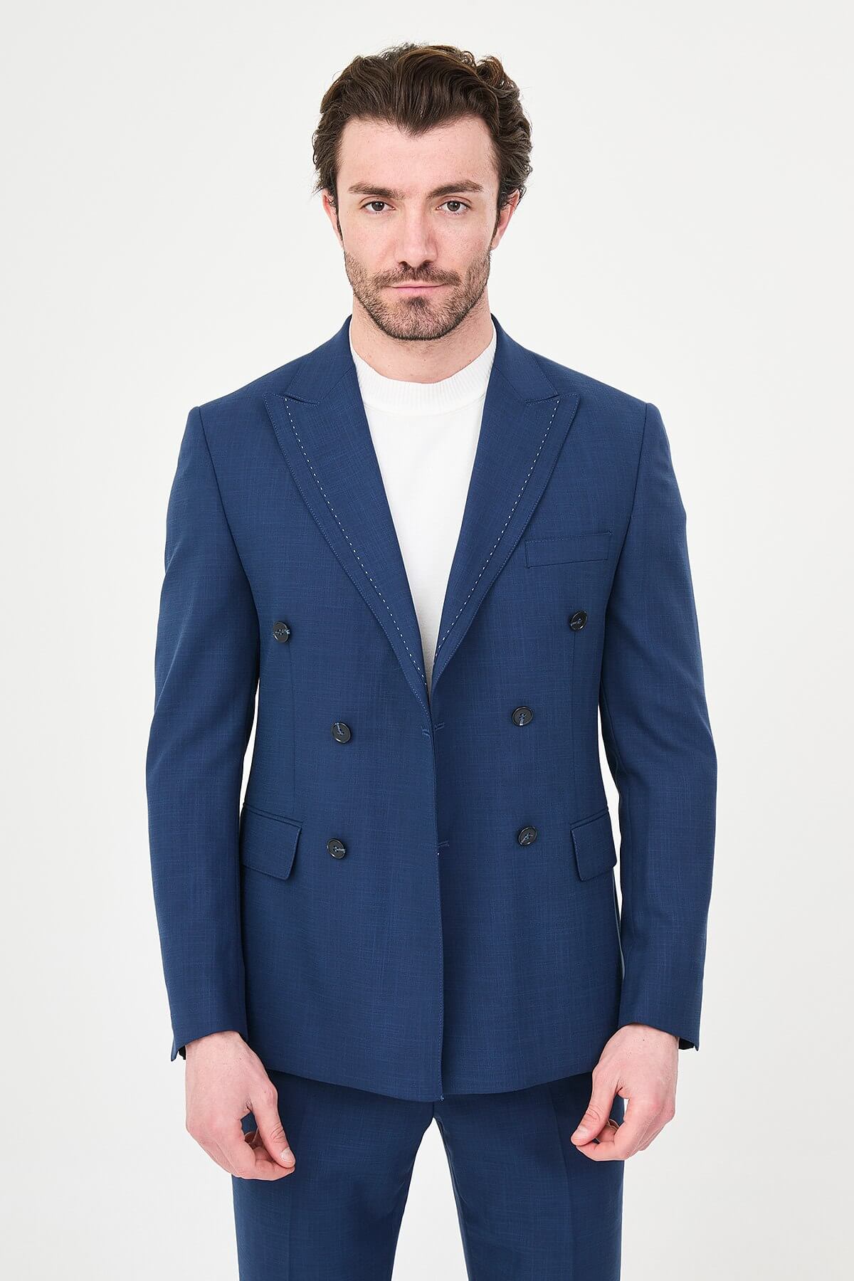 an indigo slim-fit double-breasted linen-blend suit with peak lapels, contrast pick stitching, matching trousers, a white knit top, and white leather sneakers.