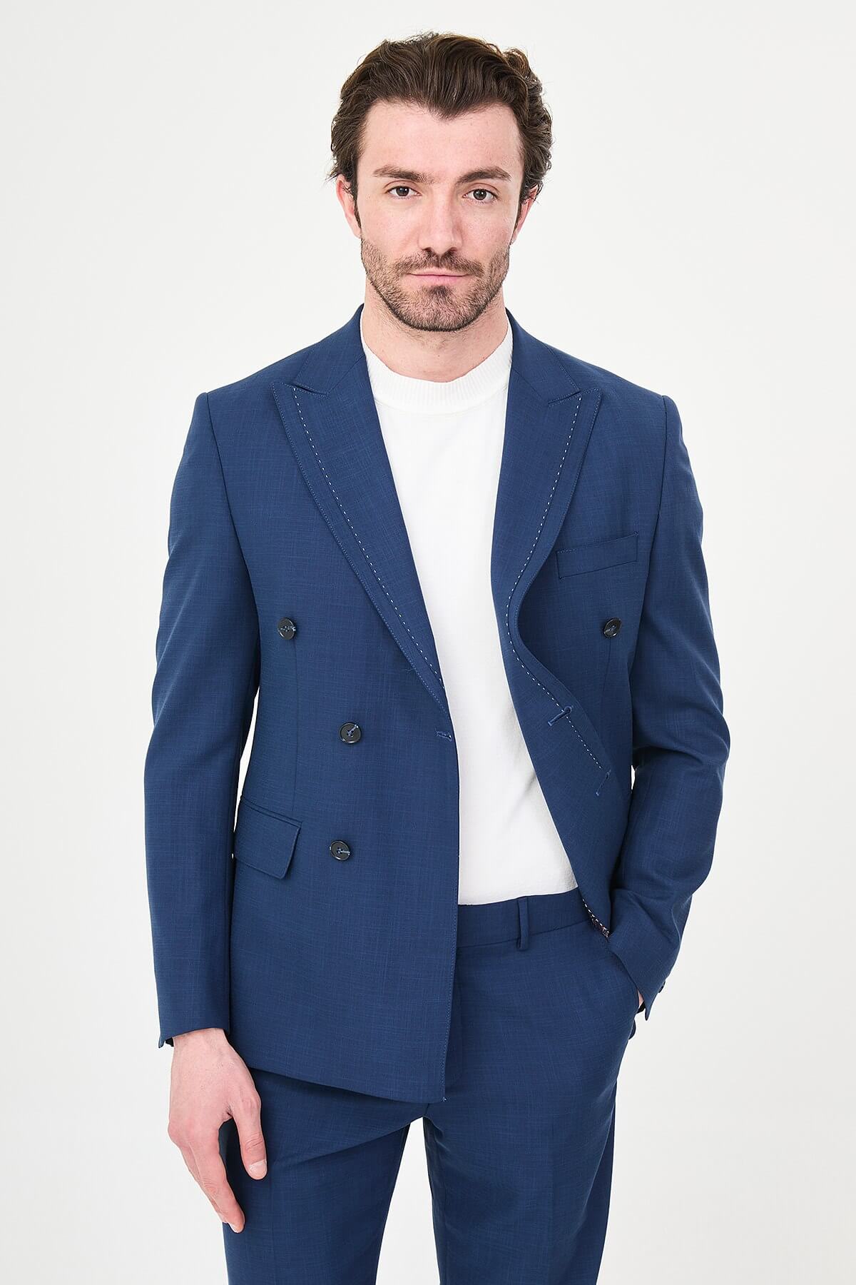 an indigo slim-fit double-breasted linen-blend suit with peak lapels, contrast pick stitching, matching trousers, a white knit top, and white leather sneakers.