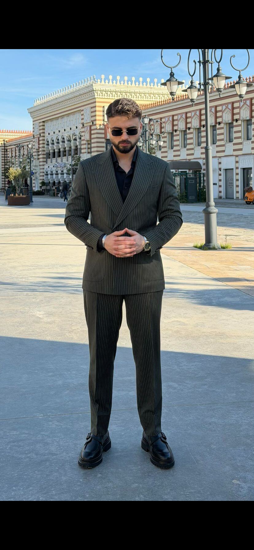 Men’s khaki pinstripe double-breasted suit styled with black shirt and loafers in a modern formal outfit outdoors