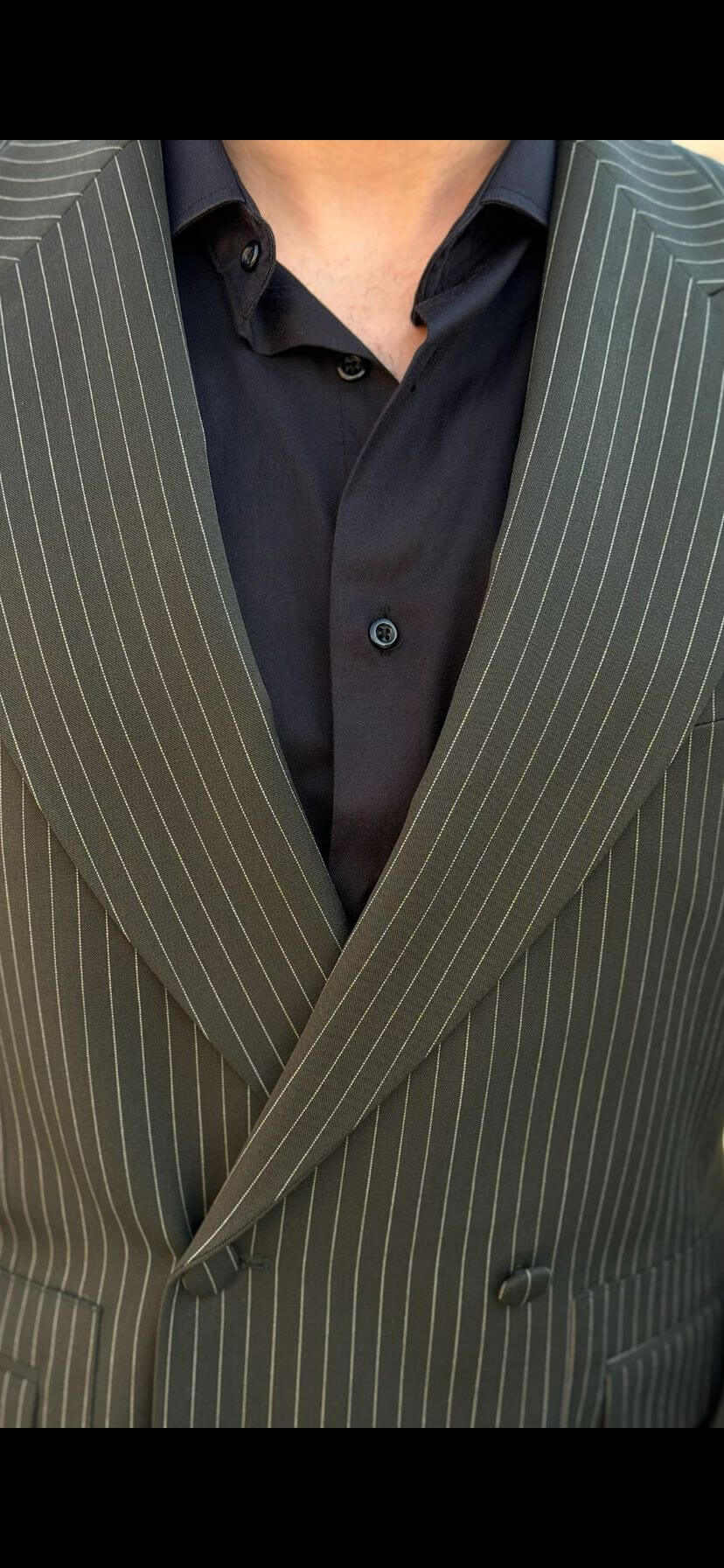 Men’s khaki pinstripe double-breasted suit styled with black shirt and loafers in a modern formal outfit outdoors