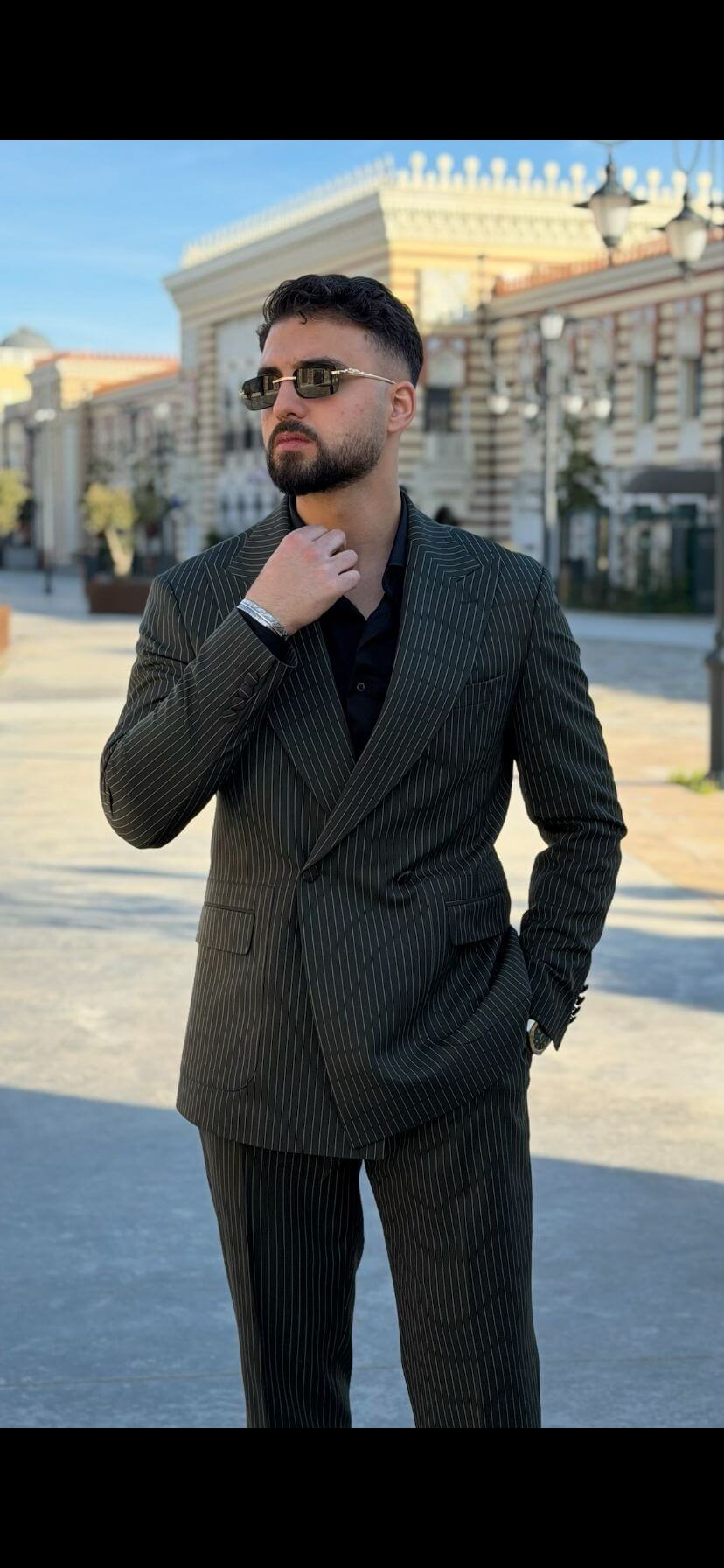 Men’s khaki pinstripe double-breasted suit styled with black shirt and loafers in a modern formal outfit outdoors