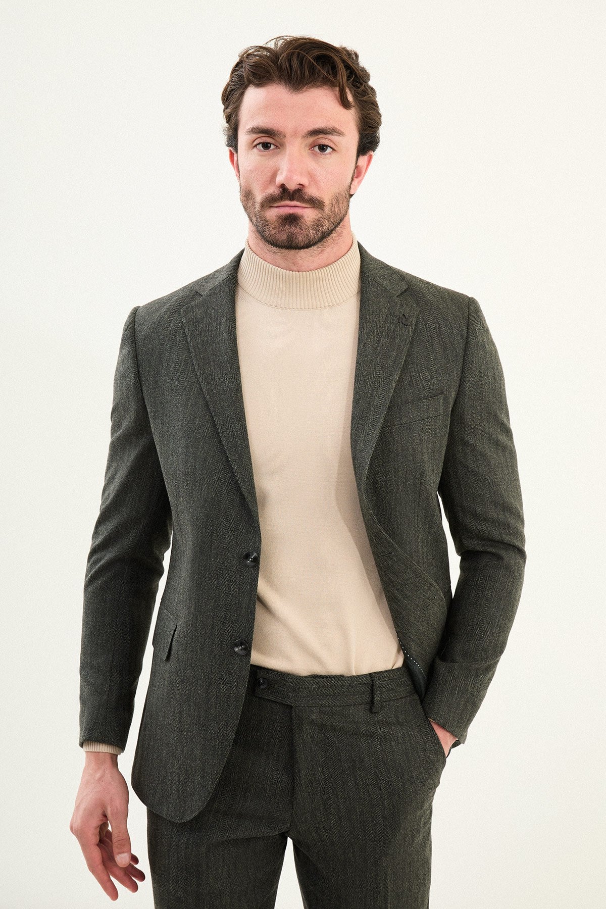 Men’s olive-toned khaki herringbone slim-fit single-breasted suit with structured shoulders and tailored waist, high-wool blend fabric with stretch for winter wear, styled with a cream fine-gauge turtleneck.