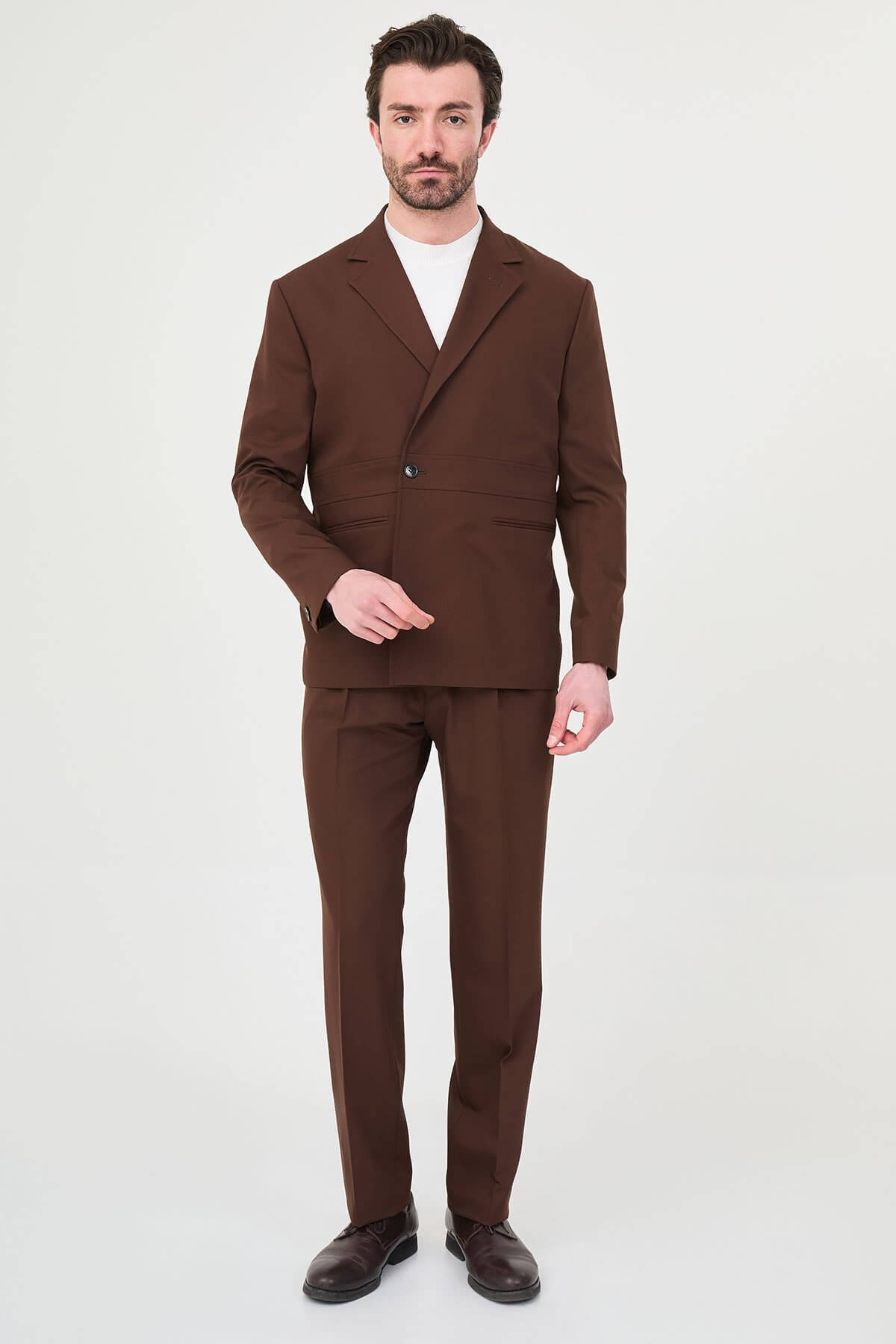 Men wearing a light brown slim fit suit with matching trousers, styled with a white crew-neck shirt, standing outdoors, showcasing a modern formal and smart-casual look.