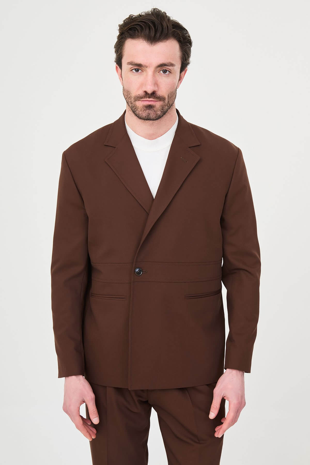 Men wearing a light brown slim fit suit with matching trousers, styled with a white crew-neck shirt, standing outdoors, showcasing a modern formal and smart-casual look.