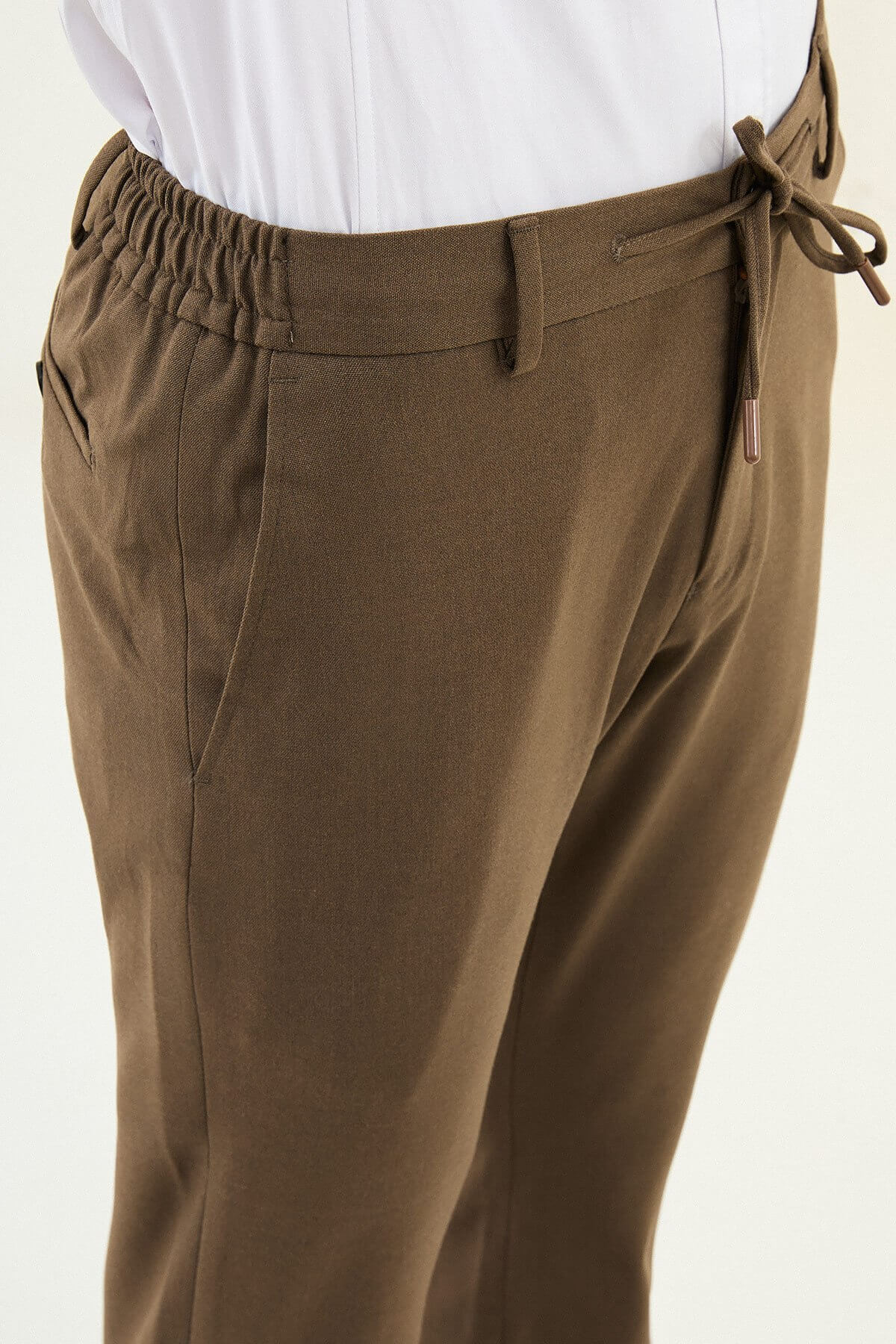 Men wearing mink slim-fit drawstring trousers with elastic waistband, styled with sneakers and dress shoes for versatile summer menswear.