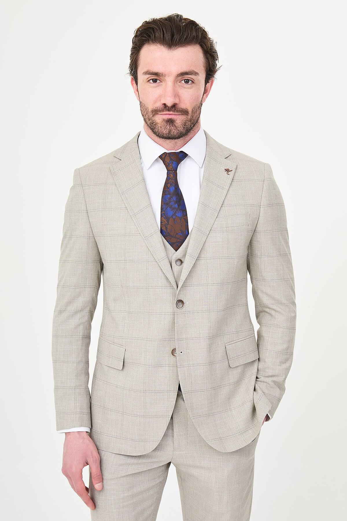a mink slim-fit three-piece suit with a fine windowpane check, matching waistcoat and trousers, white dress shirt, patterned navy and brown tie, and dark brown leather shoes.