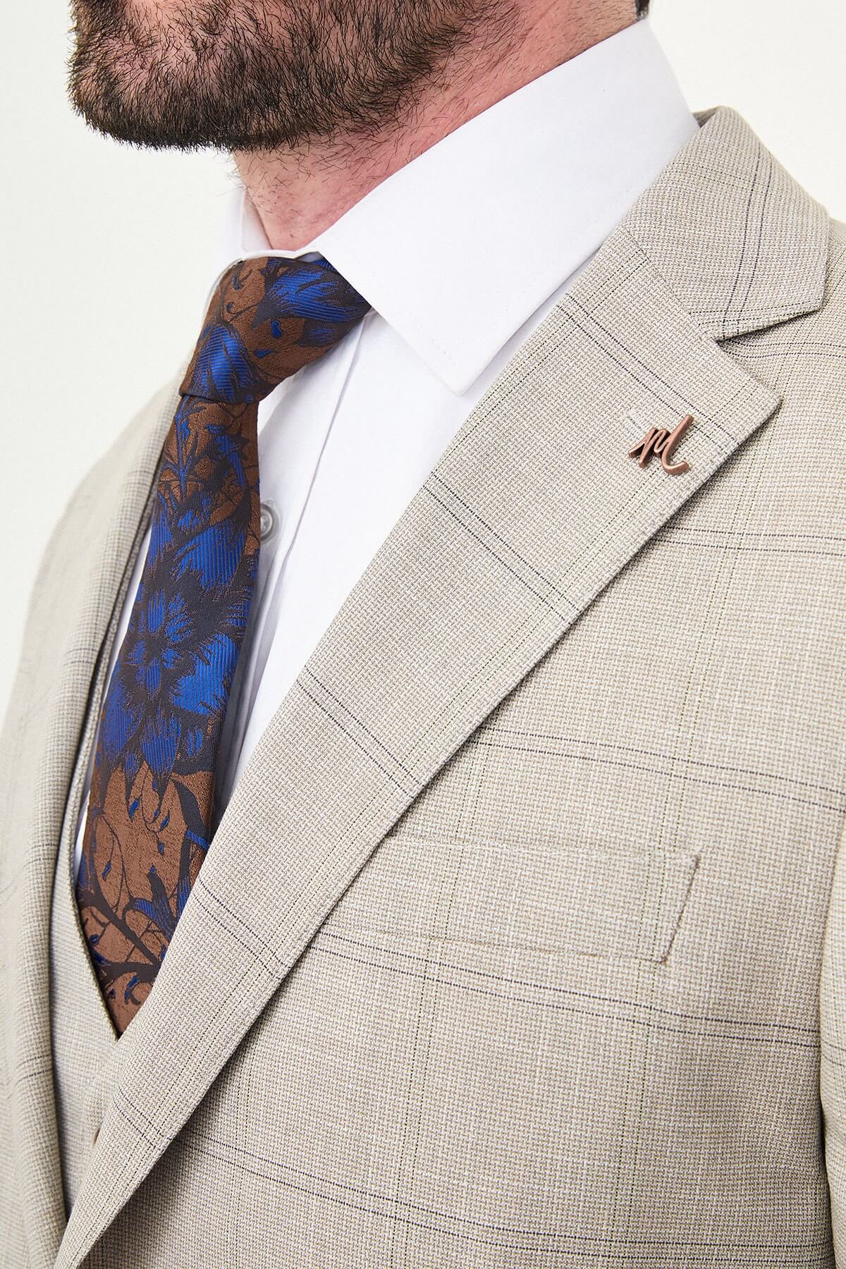a mink slim-fit three-piece suit with a fine windowpane check, matching waistcoat and trousers, white dress shirt, patterned navy and brown tie, and dark brown leather shoes.