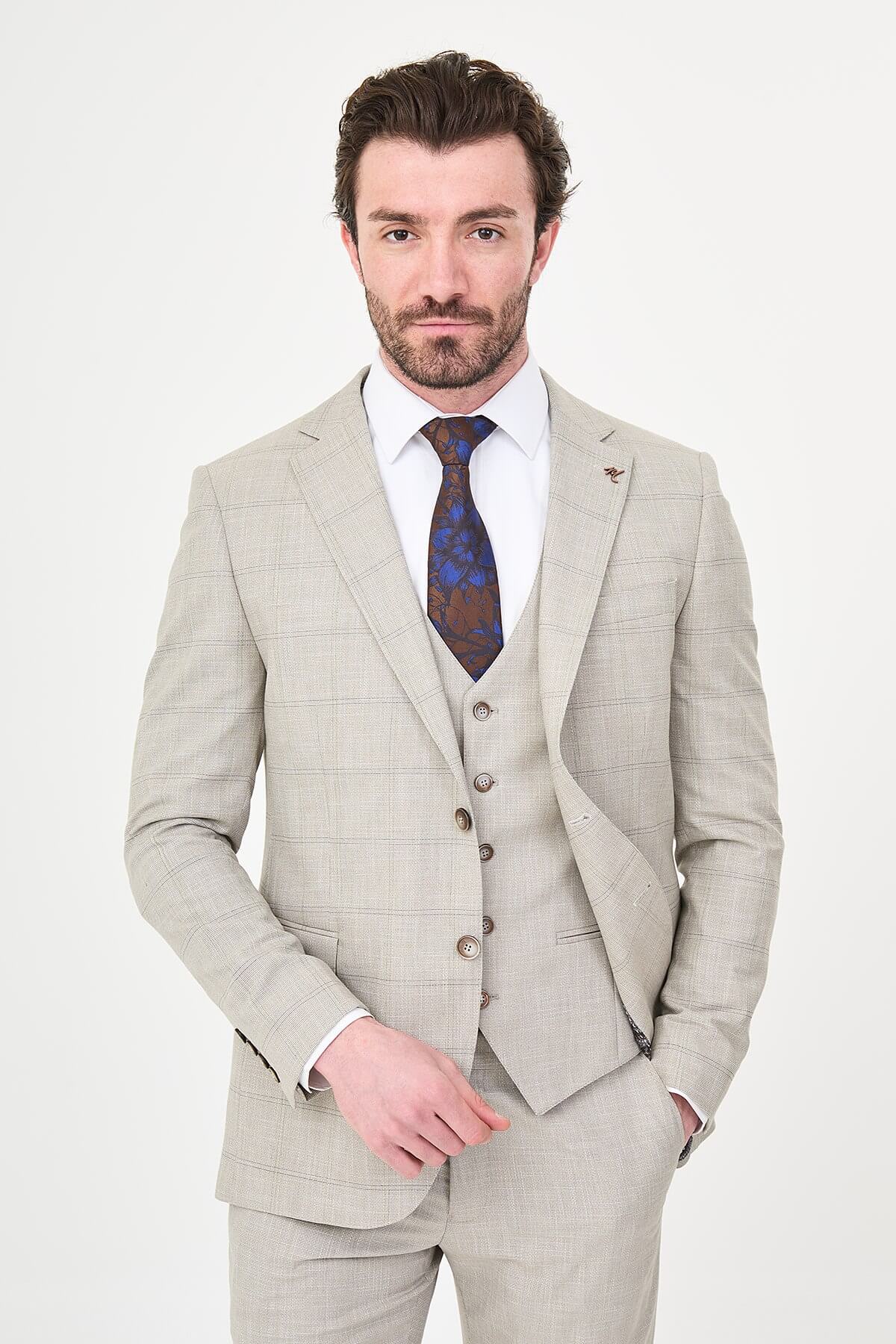 a mink slim-fit three-piece suit with a fine windowpane check, matching waistcoat and trousers, white dress shirt, patterned navy and brown tie, and dark brown leather shoes.
