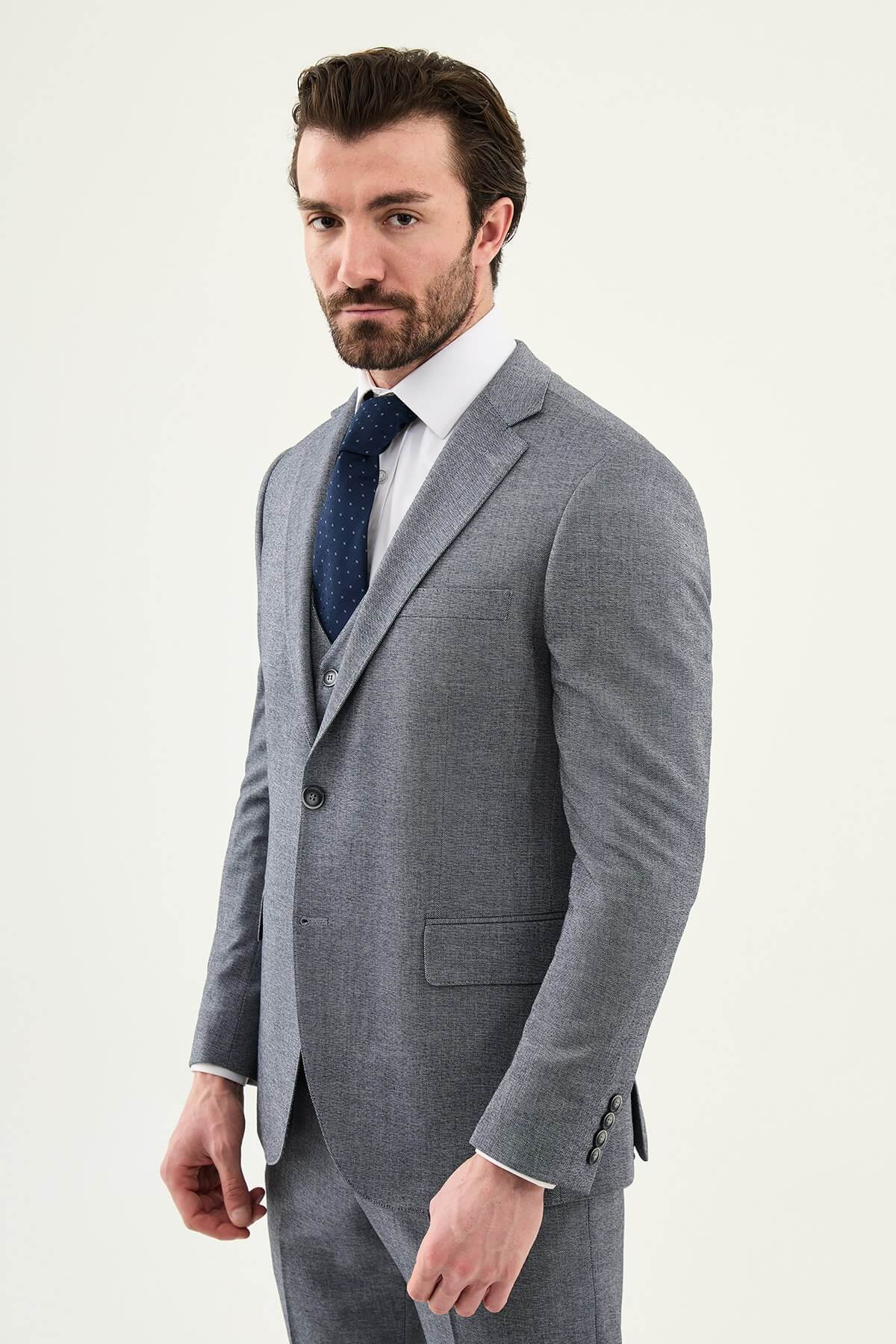 Model wearing a light grey slim-fit cotton-linen three-piece suit with a white dress shirt, navy dotted tie, and black Derby shoes.