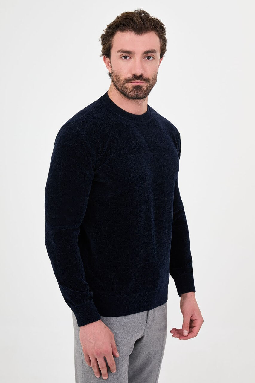 Men’s navy blue crew neck knit sweater in a cotton blend slim fit design styled with grey trousers for a refined fall winter outfit.