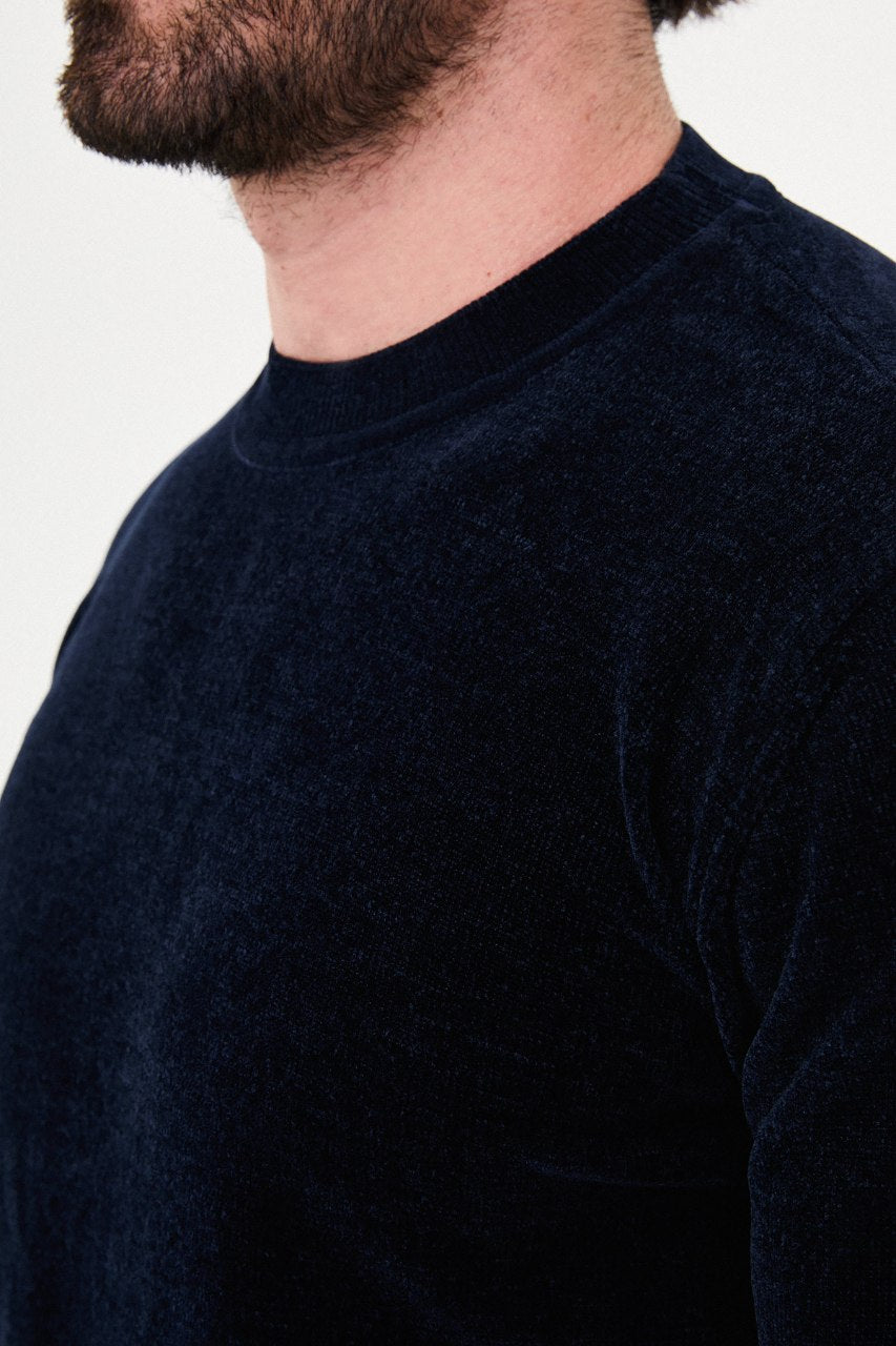 Men’s navy blue crew neck knit sweater in a cotton blend slim fit design styled with grey trousers for a refined fall winter outfit.