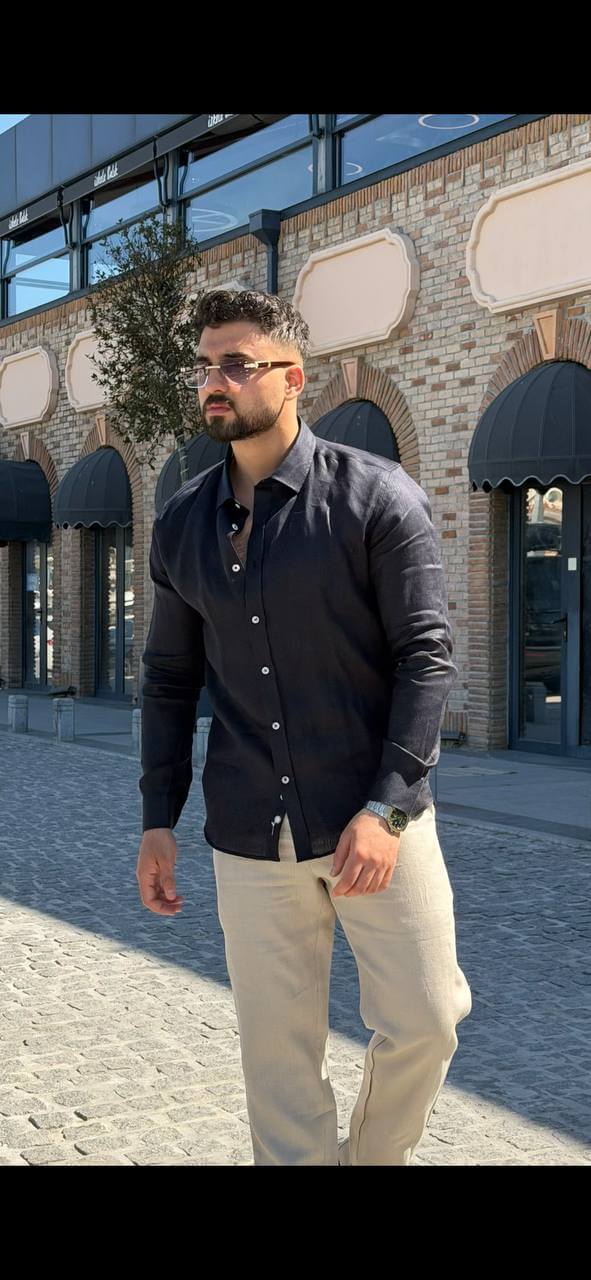 Man wearing a navy blue linen collared shirt, standing by the waterfront with sunglasses, casual summer outfit.