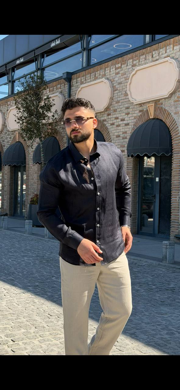 Man wearing a navy blue linen collared shirt, standing by the waterfront with sunglasses, casual summer outfit.