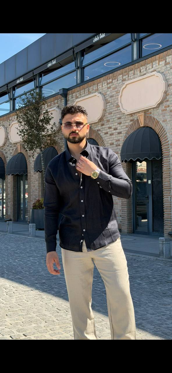 Man wearing a navy blue linen collared shirt, standing by the waterfront with sunglasses, casual summer outfit.