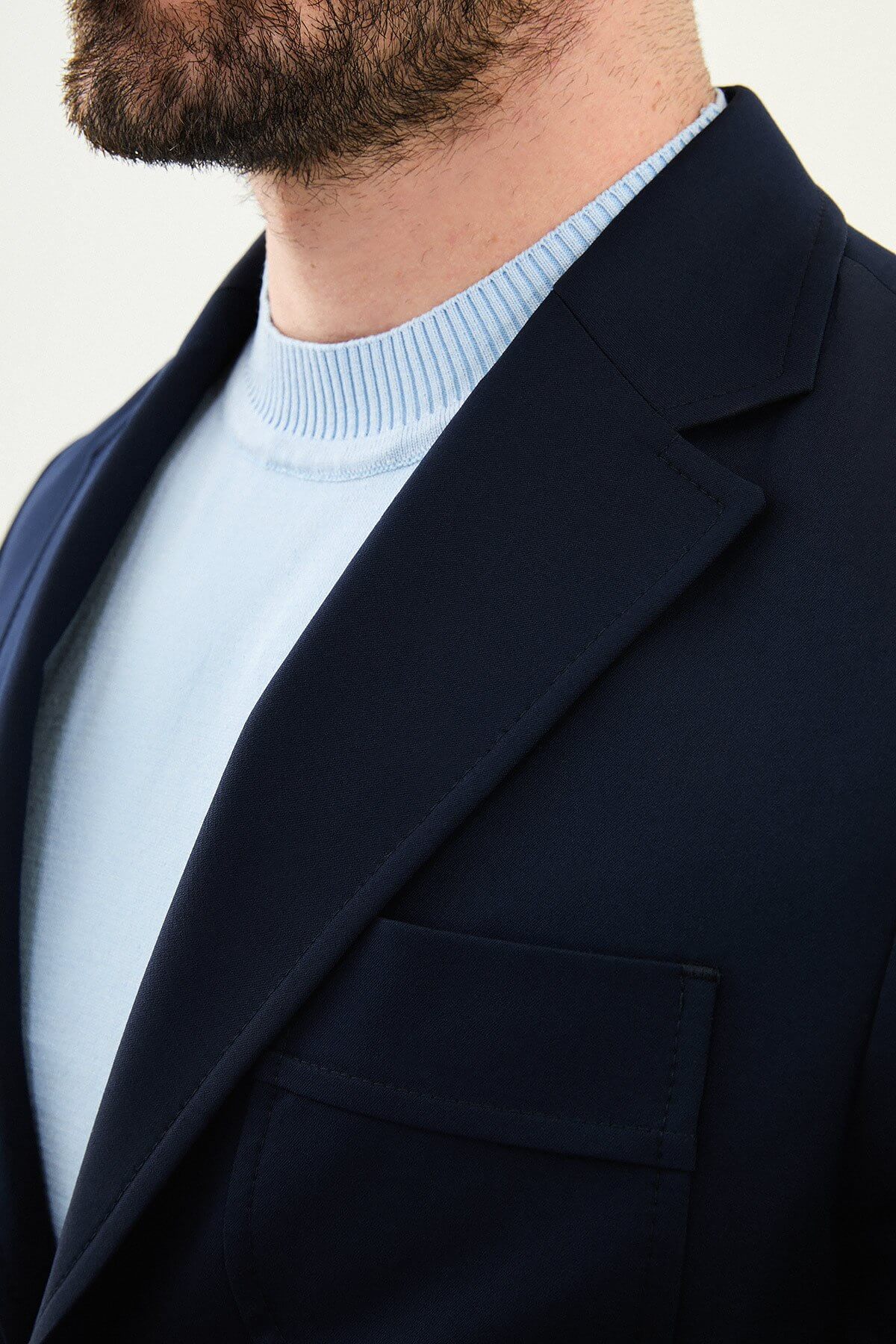 Men’s navy blue slim fit blazer with a clean modern design and stretch fabric, styled with a light blue knit top for elegant smart casual and formal occasions.