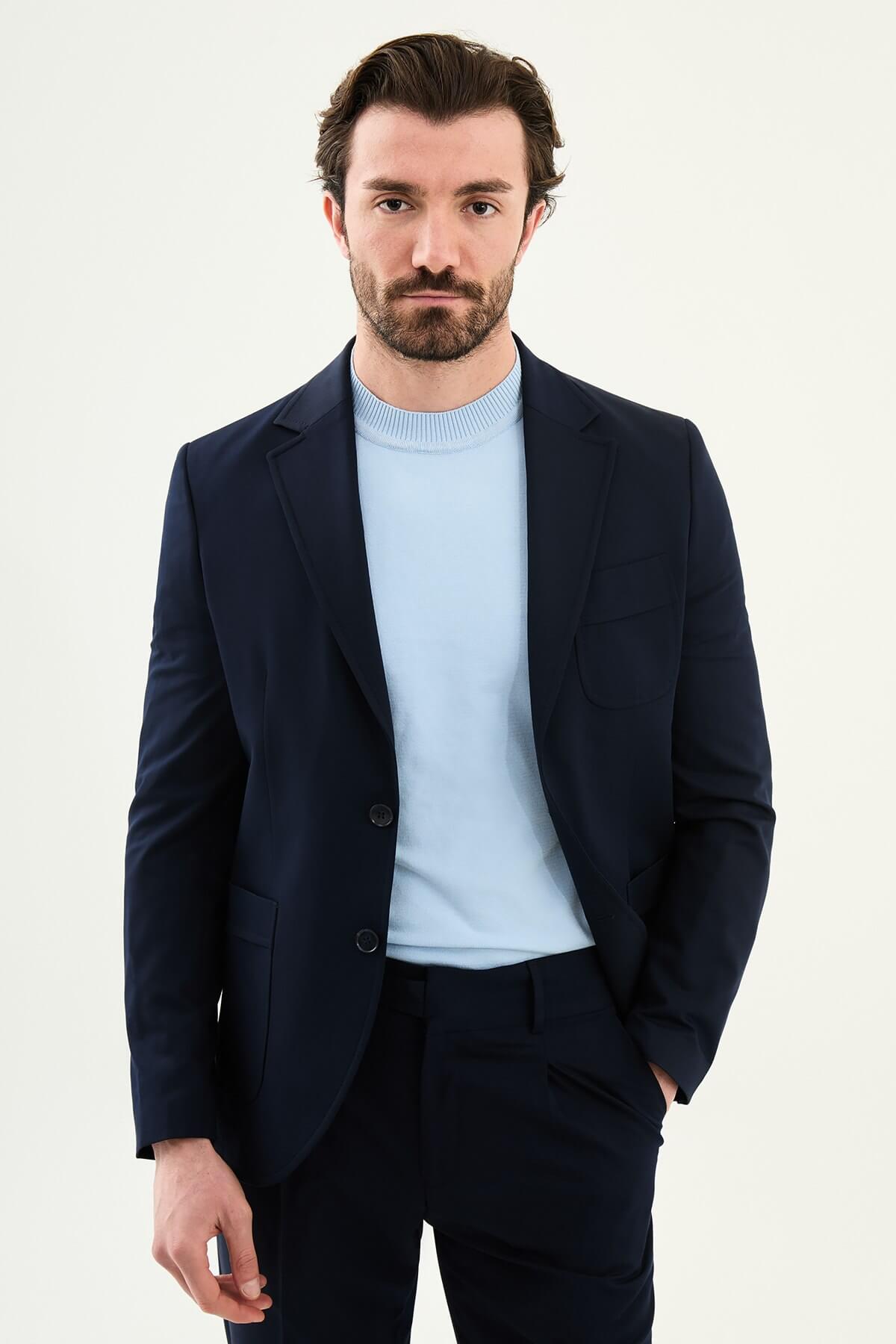 Men’s navy blue slim fit blazer with a clean modern design and stretch fabric, styled with a light blue knit top for elegant smart casual and formal occasions.
