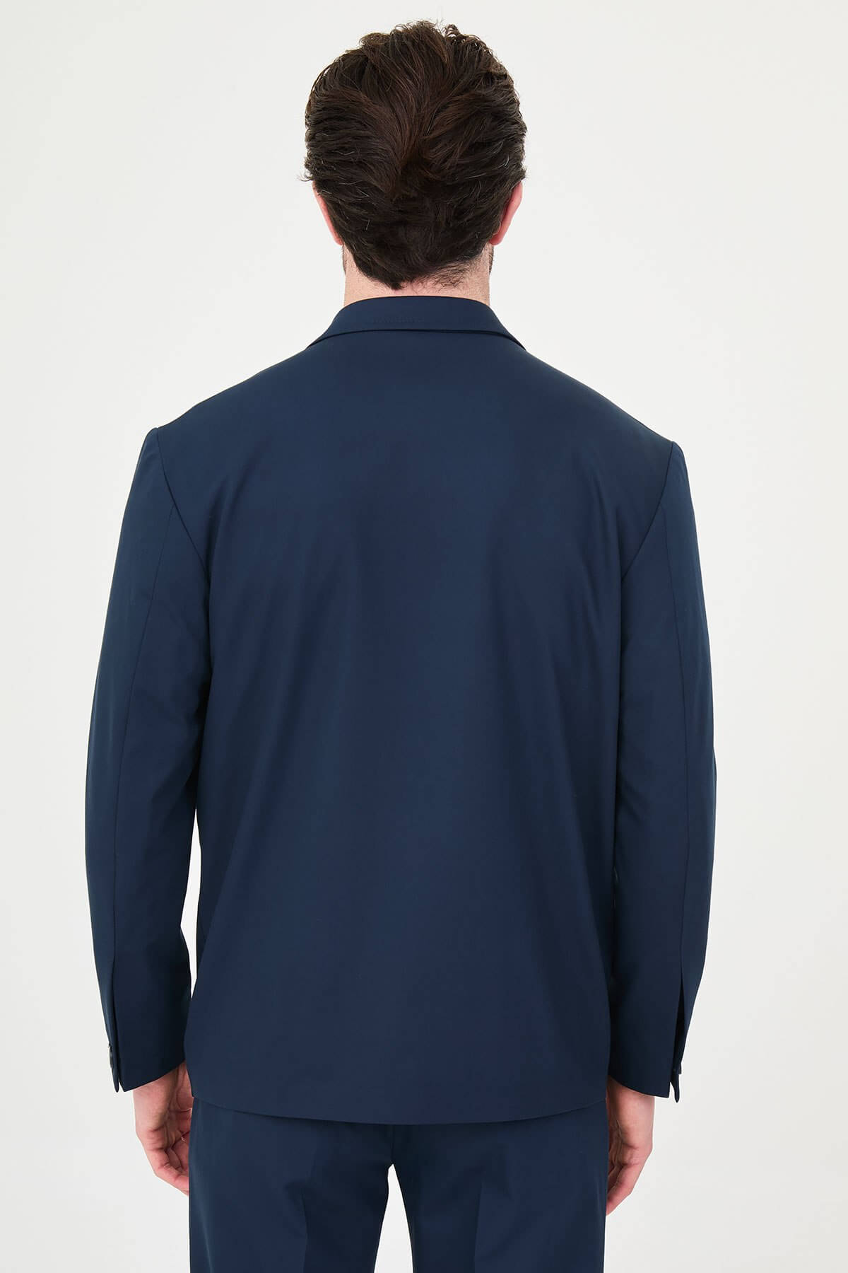 Man wearing a navy blue slim fit suit with black dress shoes, standing in a minimalist studio background, showcasing formal and elegant business attire.