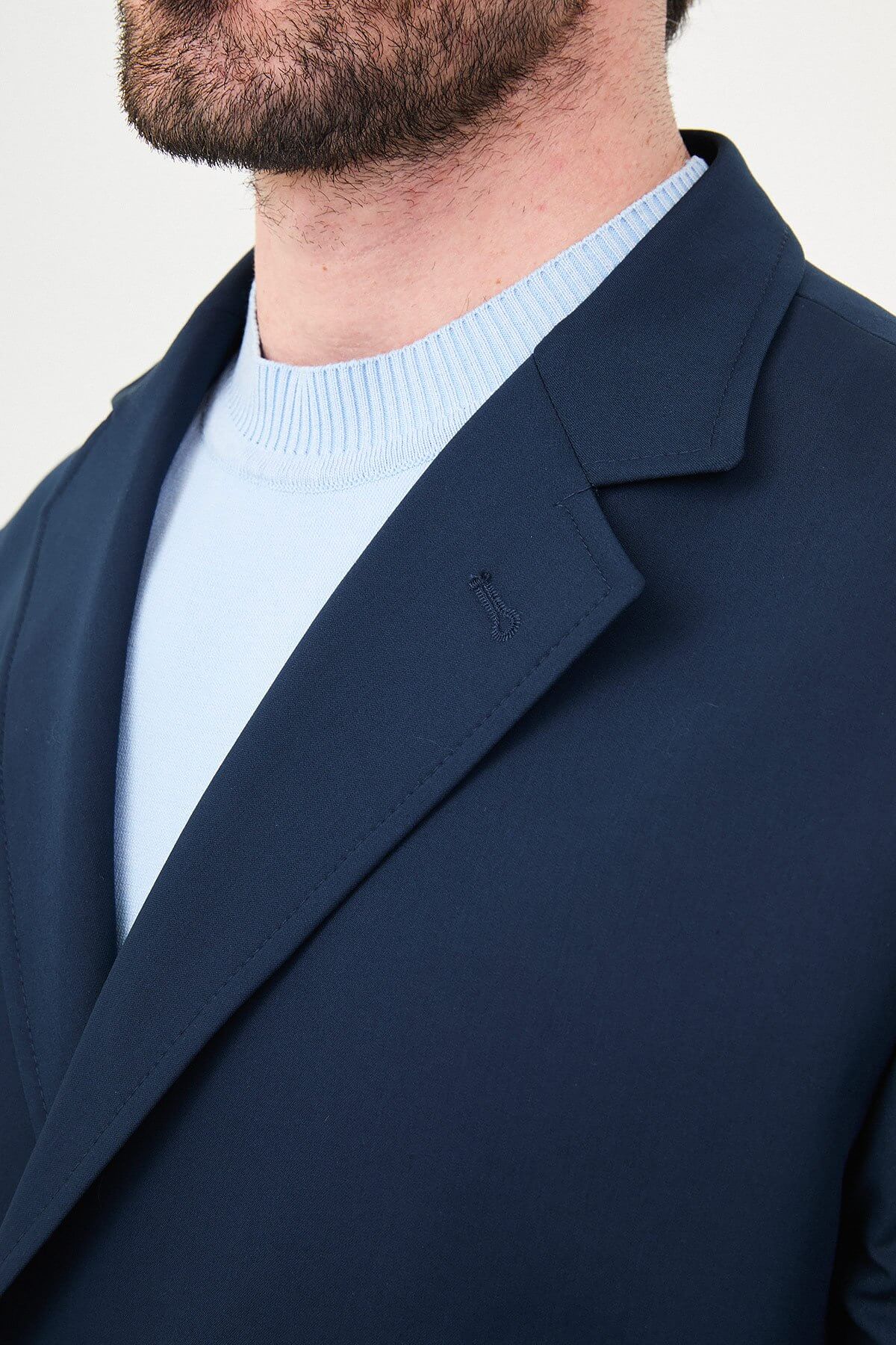 Man wearing a navy blue slim fit suit with black dress shoes, standing in a minimalist studio background, showcasing formal and elegant business attire.